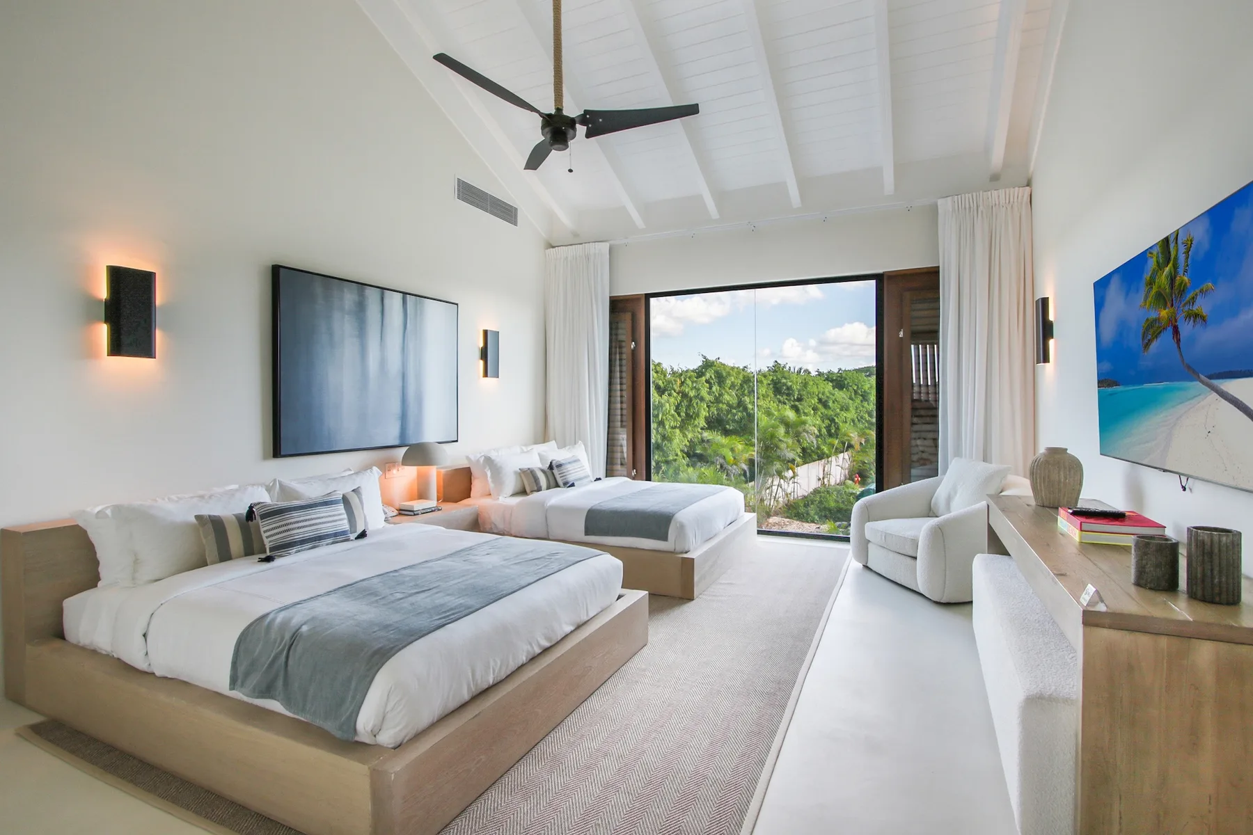 A bright bedroom with two beds, a ceiling fan, and sliding glass doors.