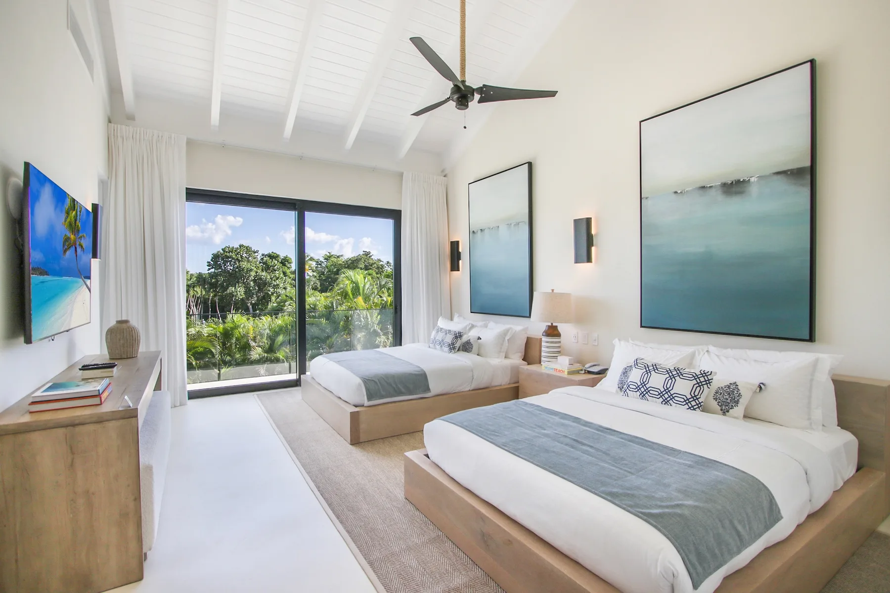 A bright bedroom with two beds, large windows, and a ceiling fan.
