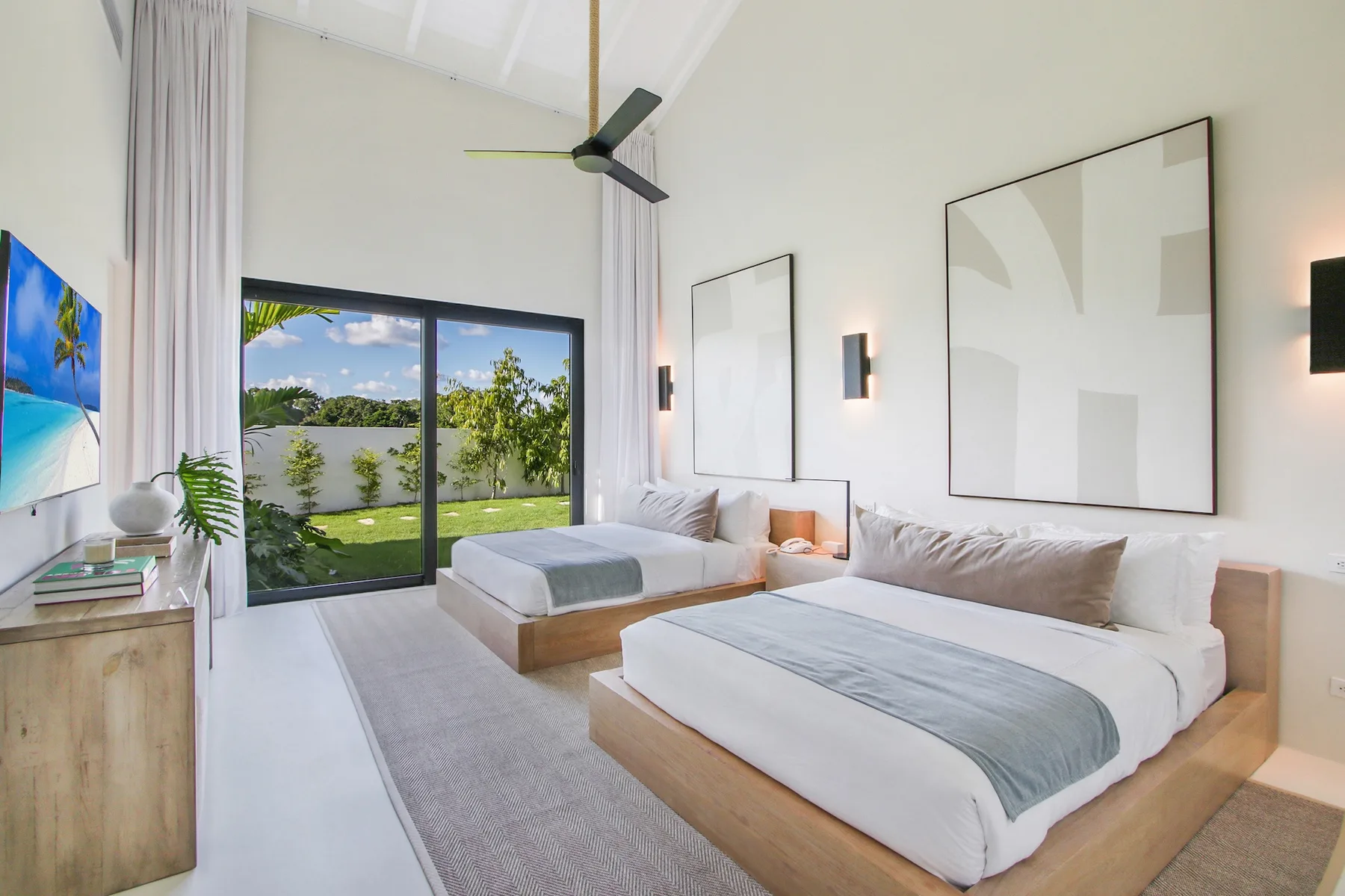 A bright bedroom with two beds and sliding glass doors opening onto a garden.
