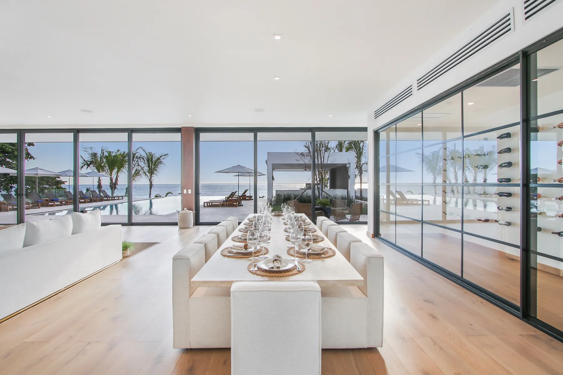 A bright dining area with a long table set beside large glass windows.