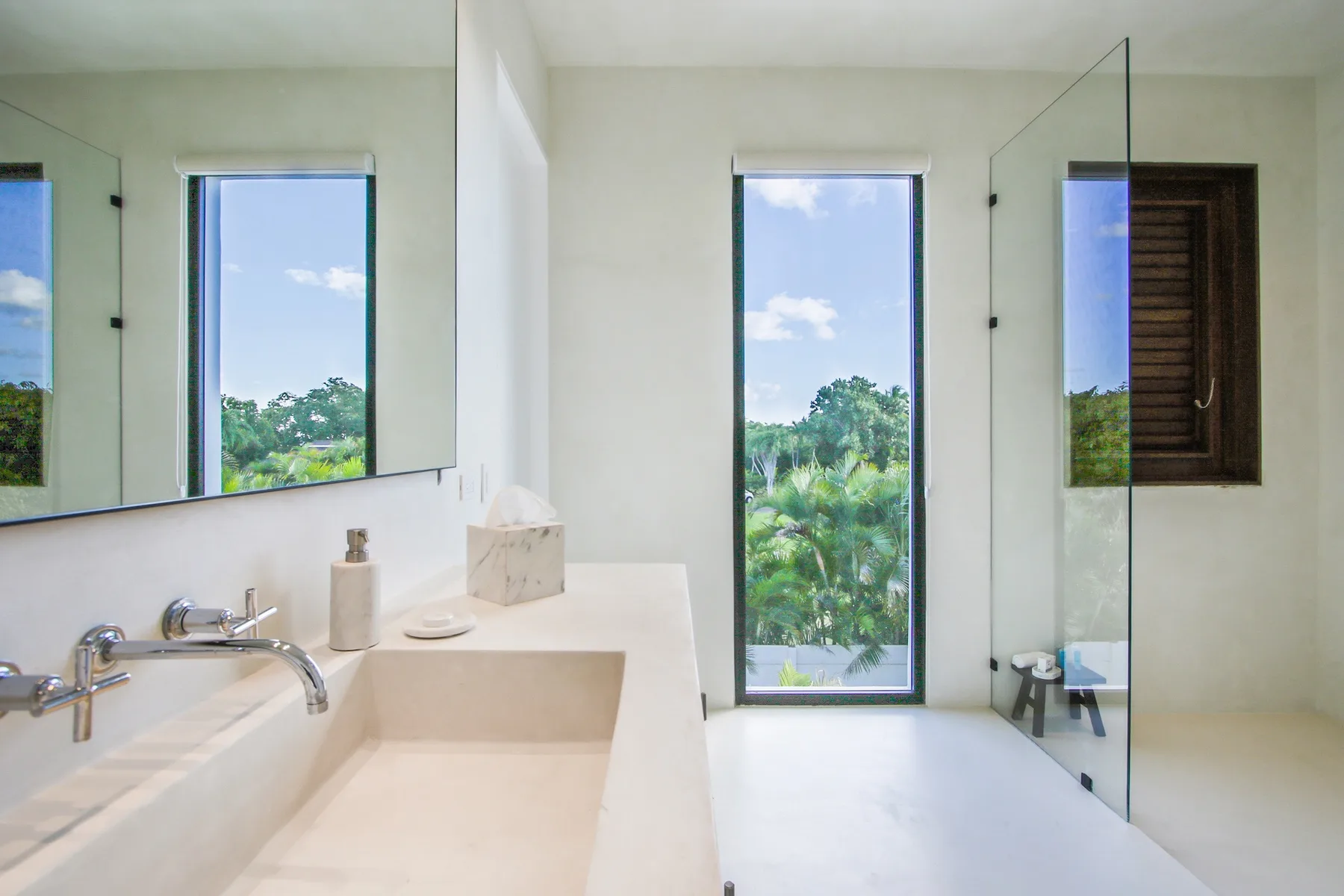 A bright bathroom with a sink, mirror, and tall window overlooking greenery.