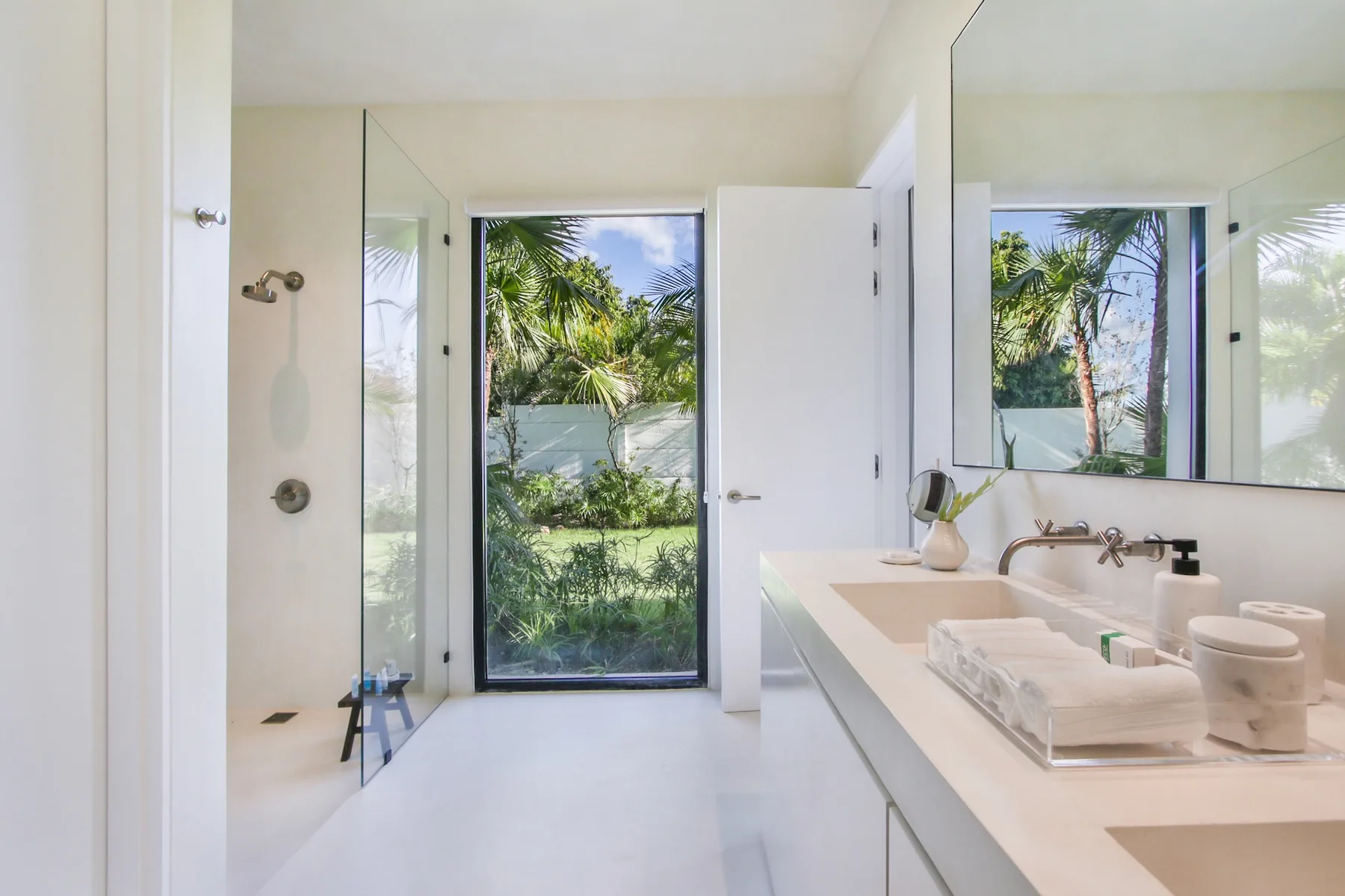A bright bathroom with a walk-in shower and a long vanity overlooking tropical greenery.