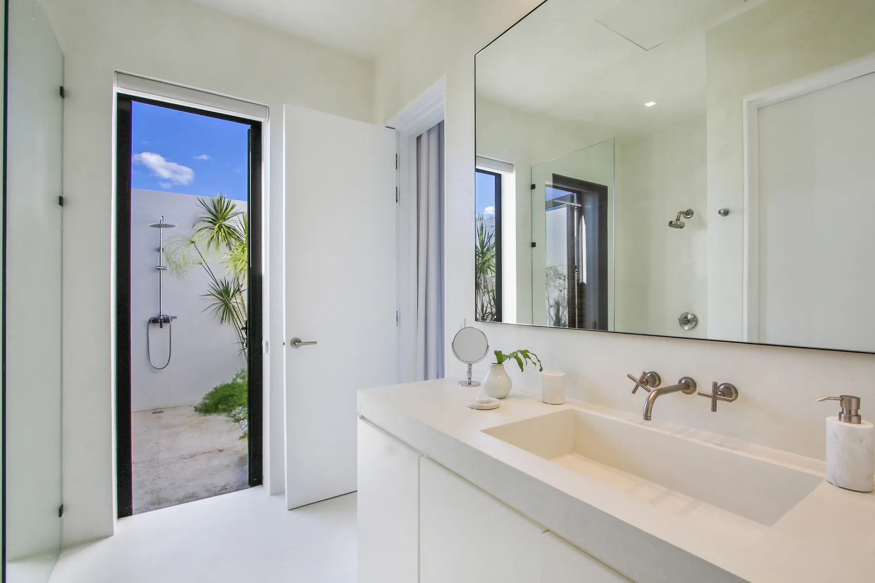 A bright bathroom with a long vanity, mirror, and shower.