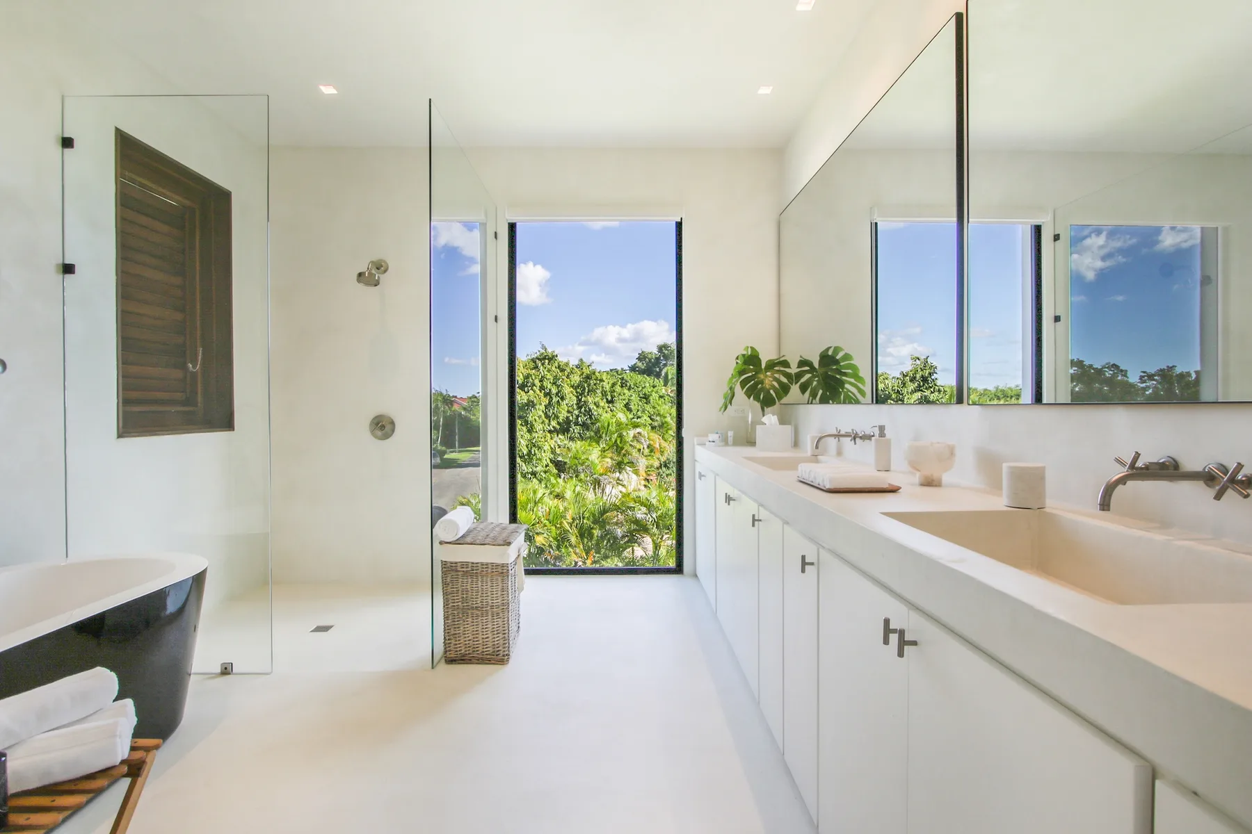 A bright bathroom with a glass shower, a bathtub, and a long vanity.