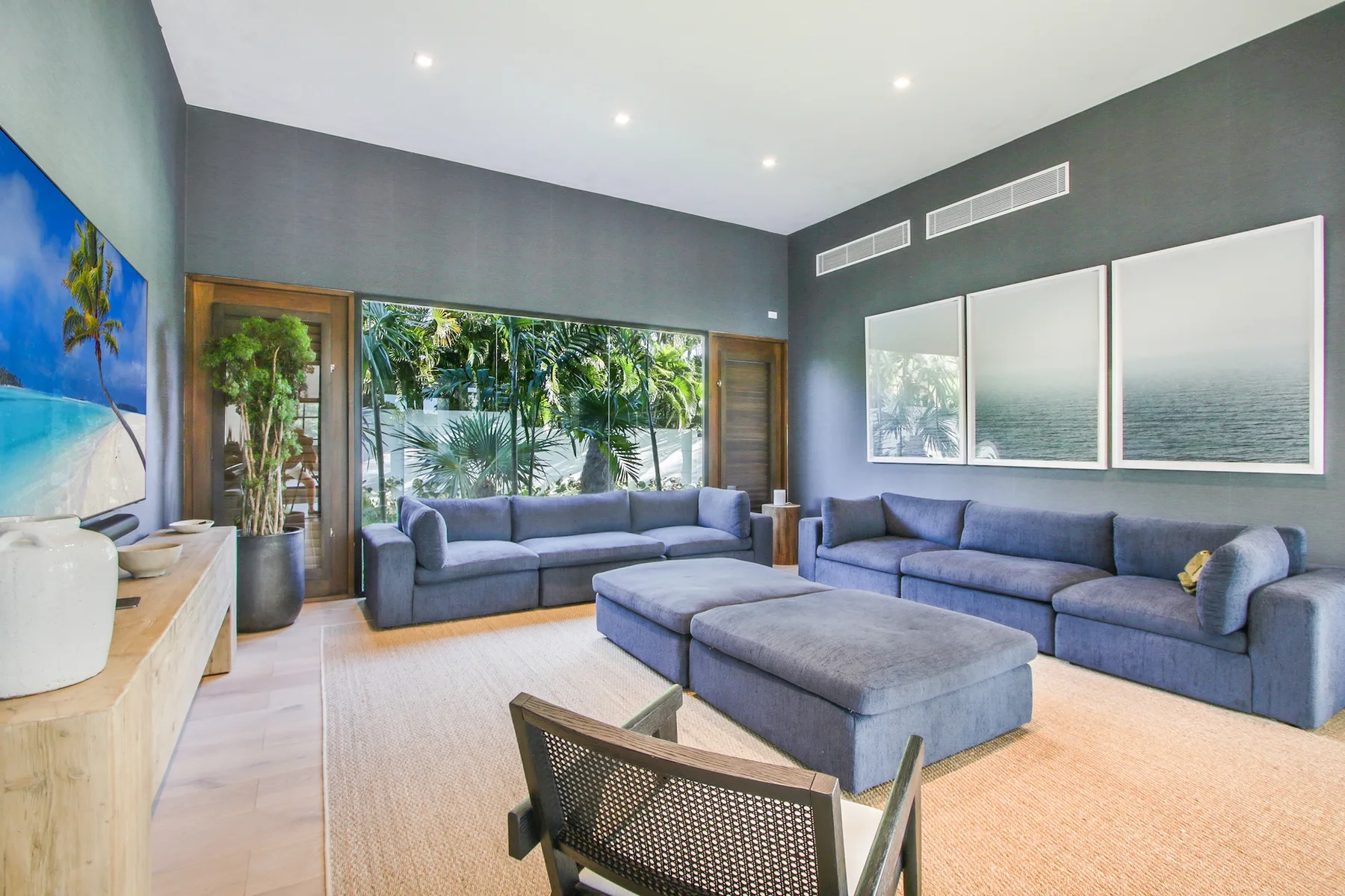 A living room with blue seating and large windows overlooking greenery.