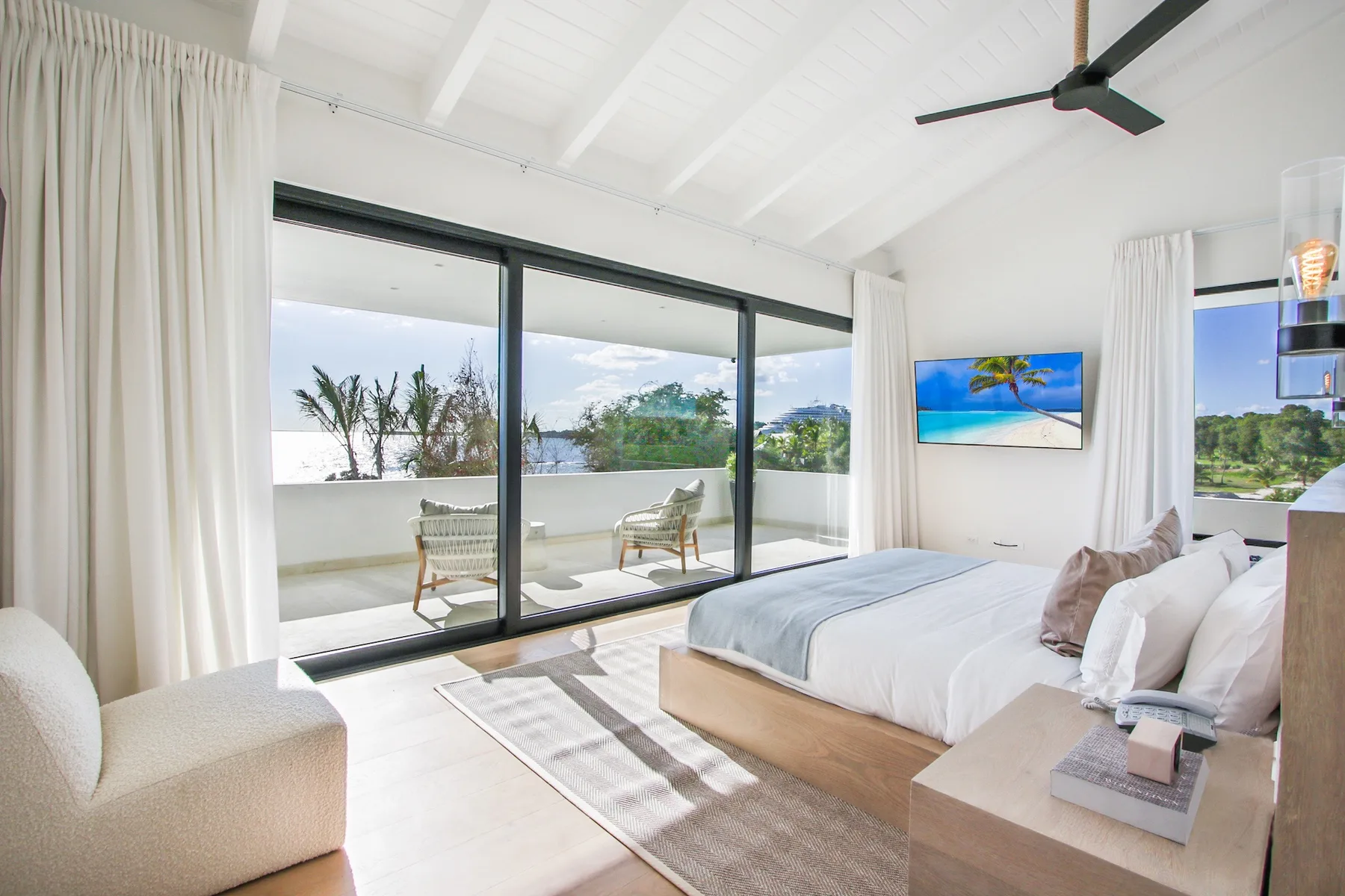 A bright bedroom with a bed beside large sliding glass doors opening onto a balcony.