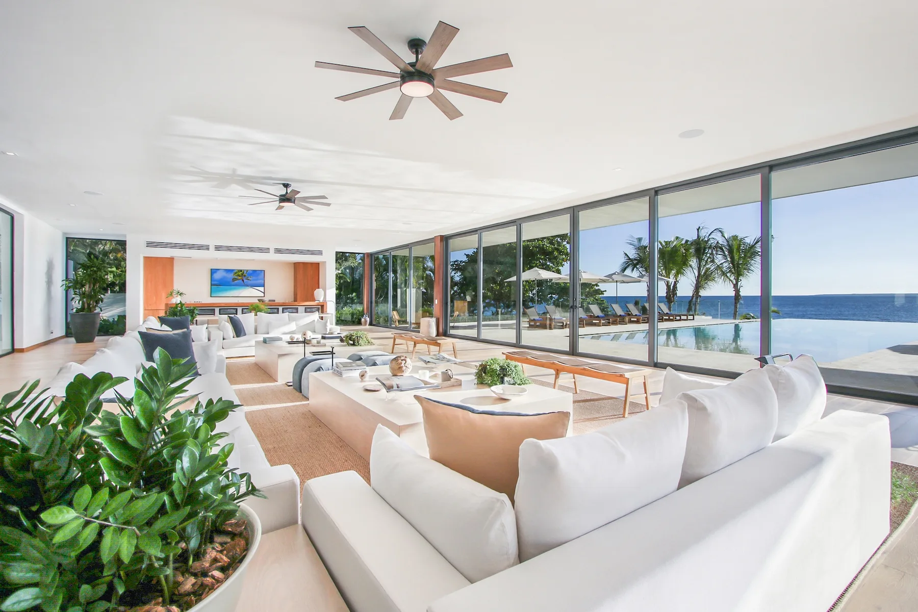 A bright living room with seating beside floor-to-ceiling windows overlooking the ocean.