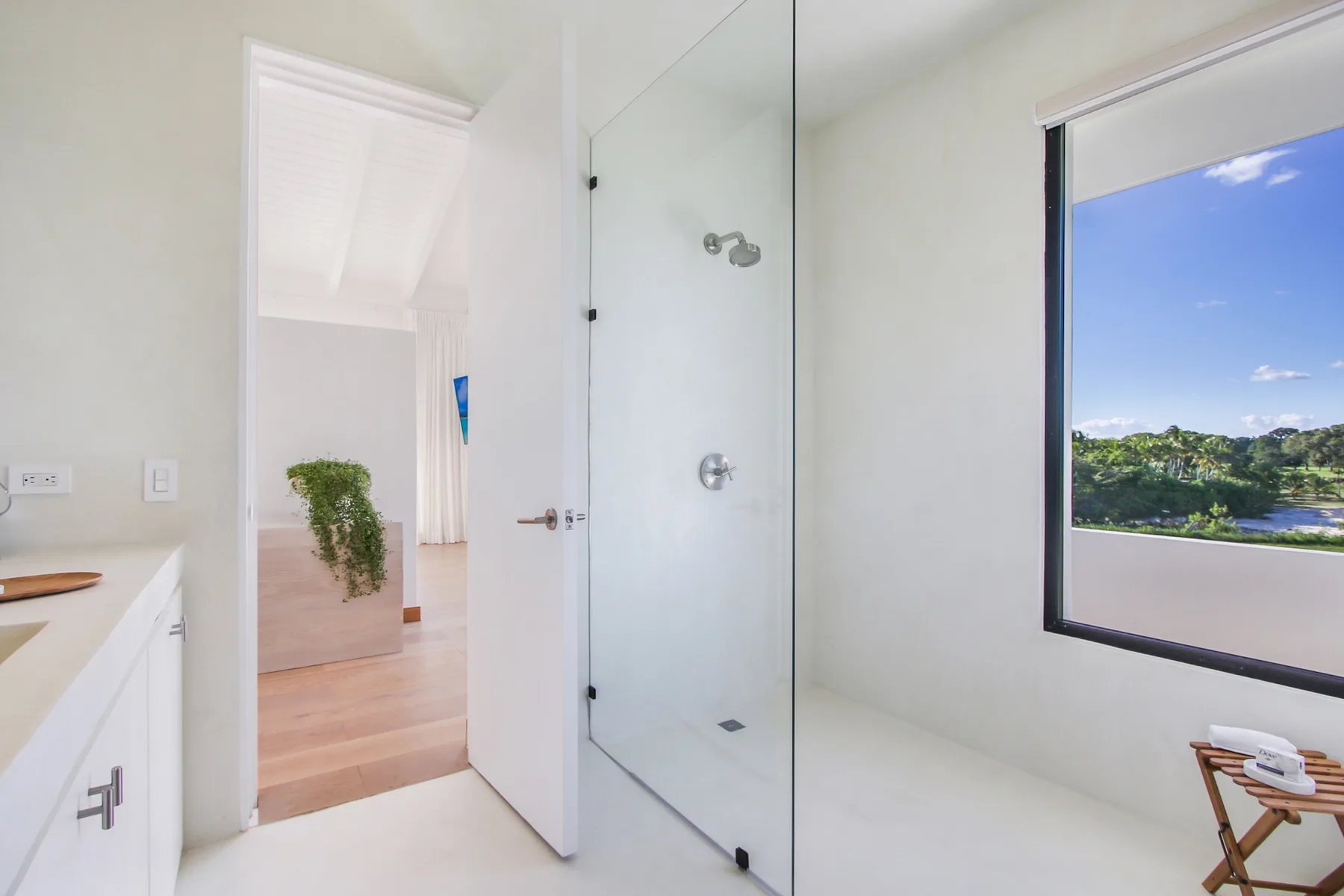 A bright bathroom with a glass shower and a large window overlooking greenery.