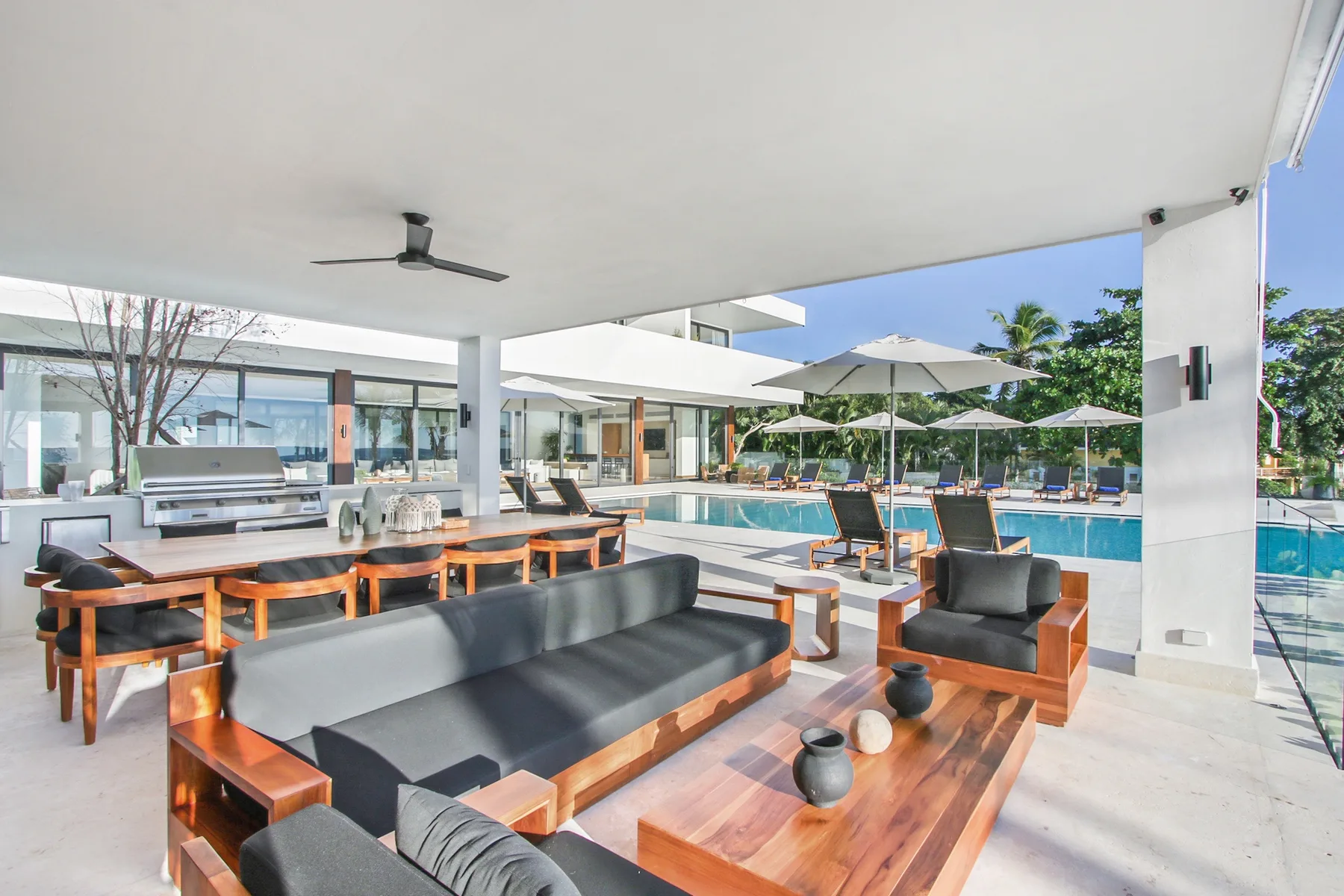 A covered outdoor lounge with seating and a pool in the background.
