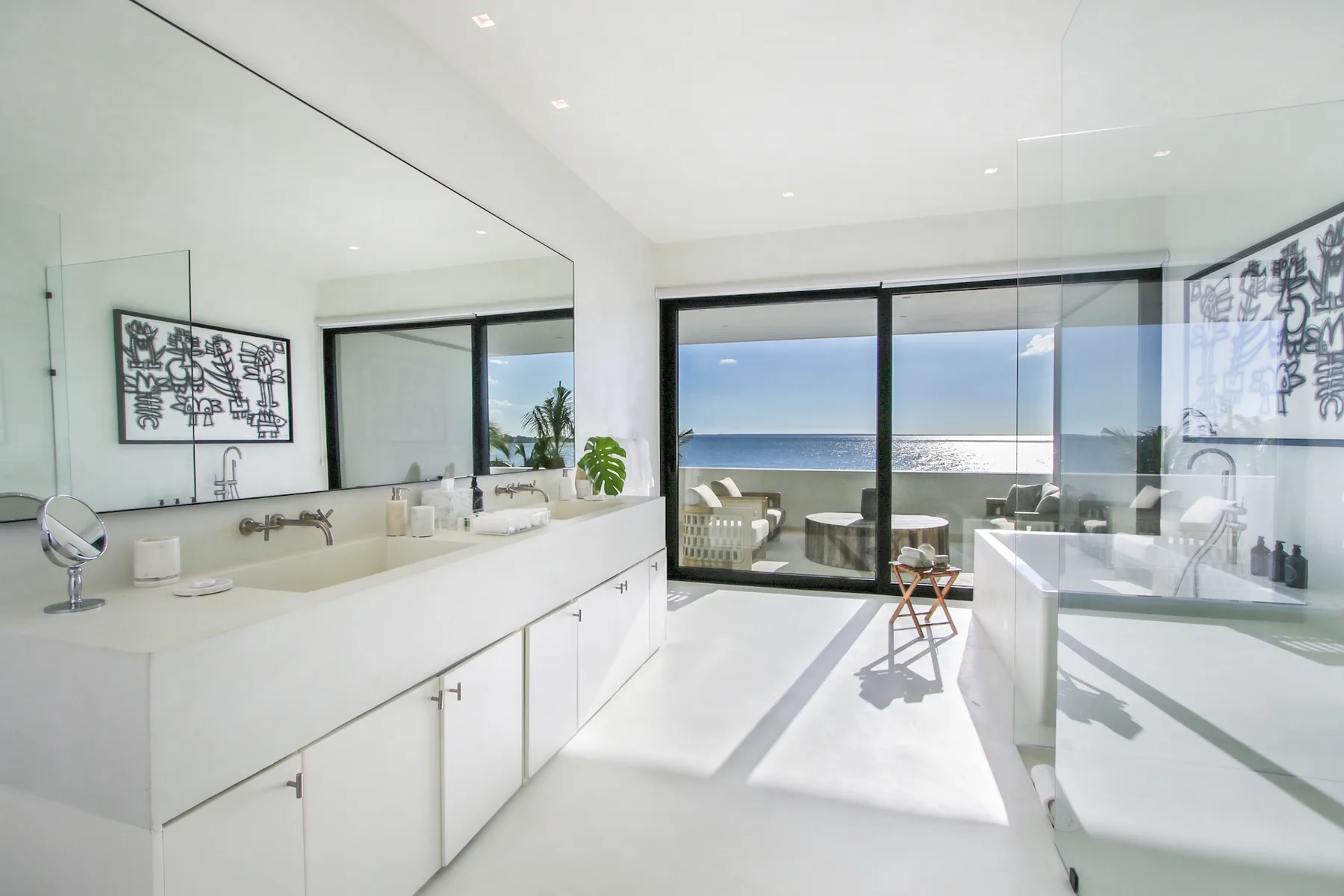 A bright bathroom opens onto a sea view through wide glass doors.