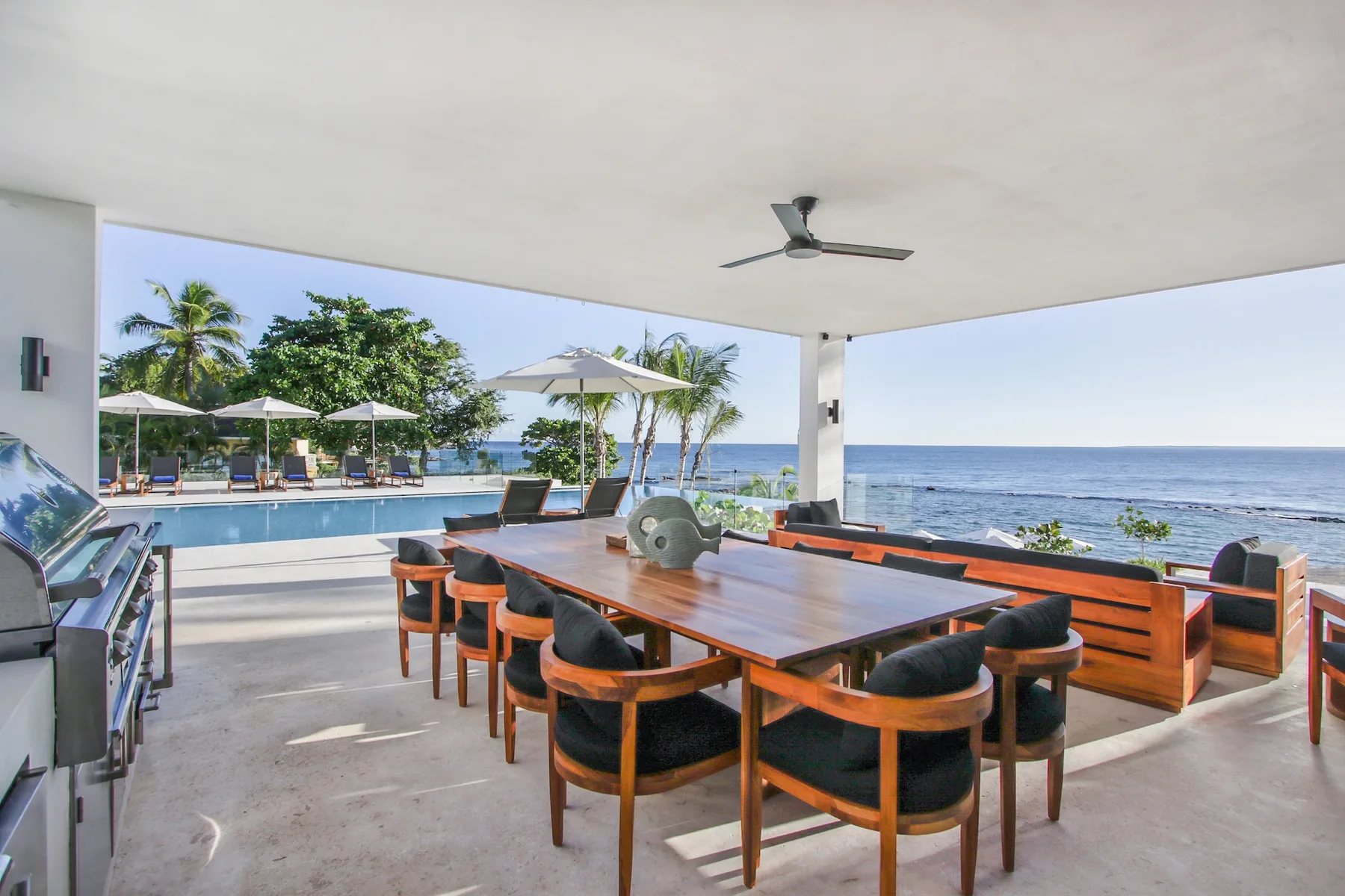 A covered seaside dining area with a long table and chairs overlooking the ocean.