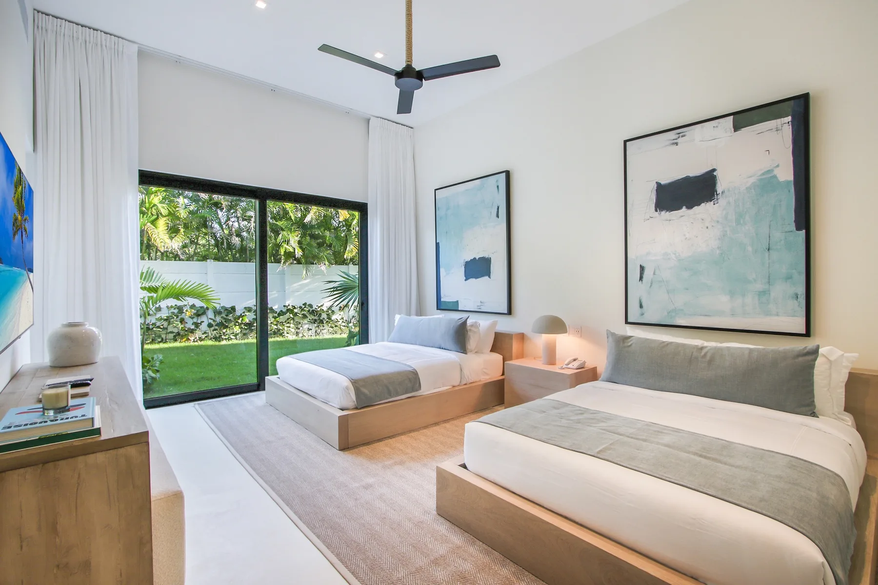 A bright bedroom with two beds, large windows, and garden views.