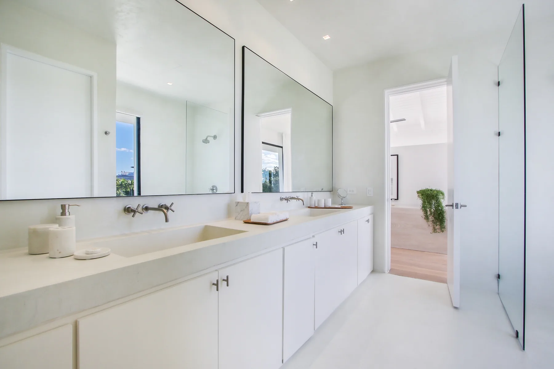 A bright bathroom vanity with white cabinets and large wall mirrors.