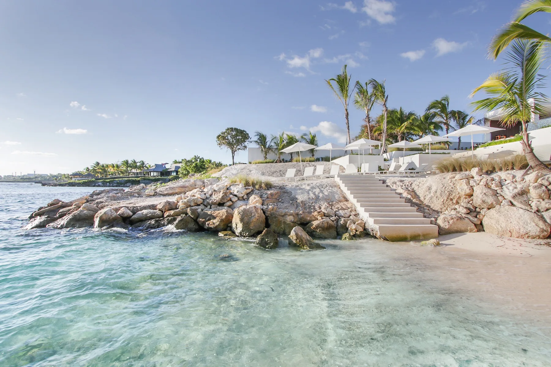 A tropical beachfront with stone steps leading from a terrace to the clear water.
