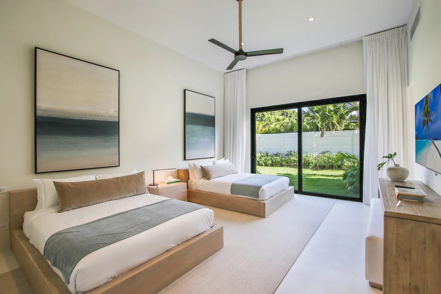 A bright bedroom with two beds and large windows overlooking a garden.