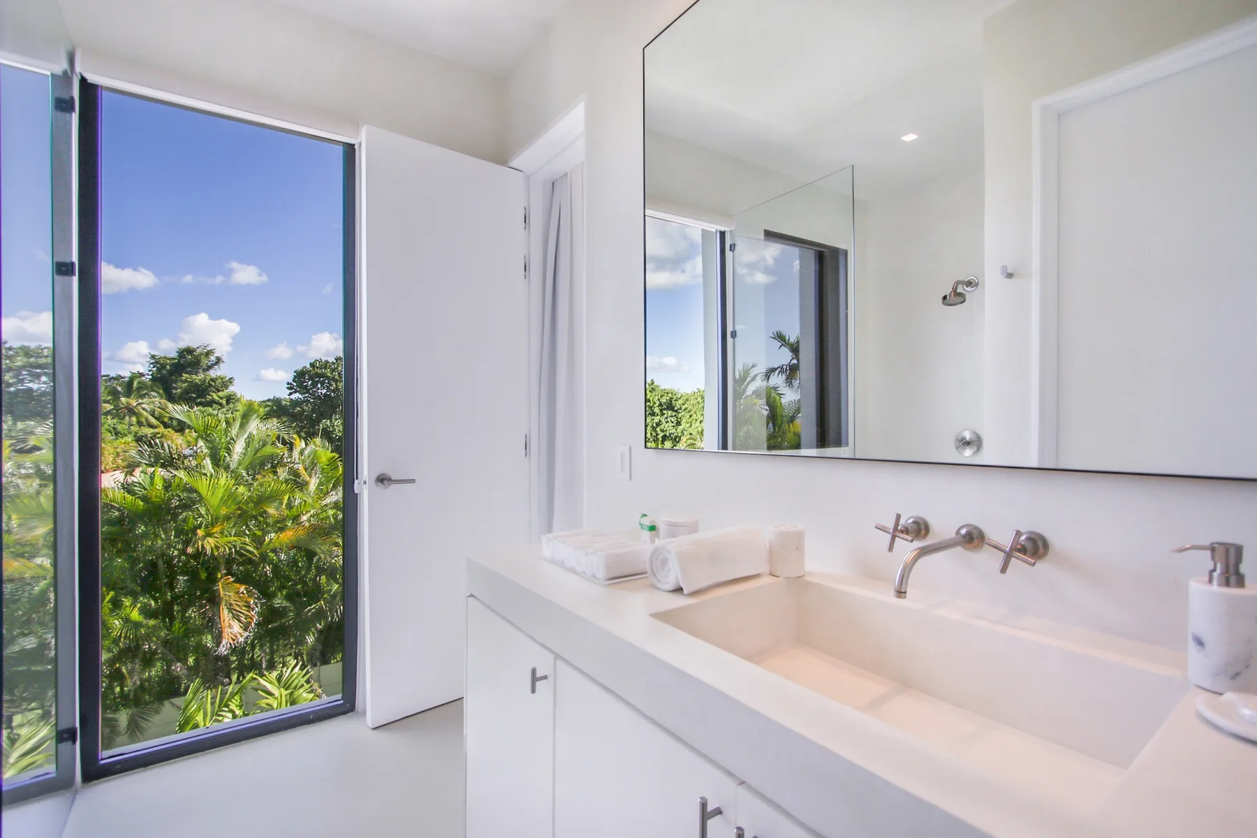 A bright bathroom with a wide sink counter and a large window overlooking greenery.