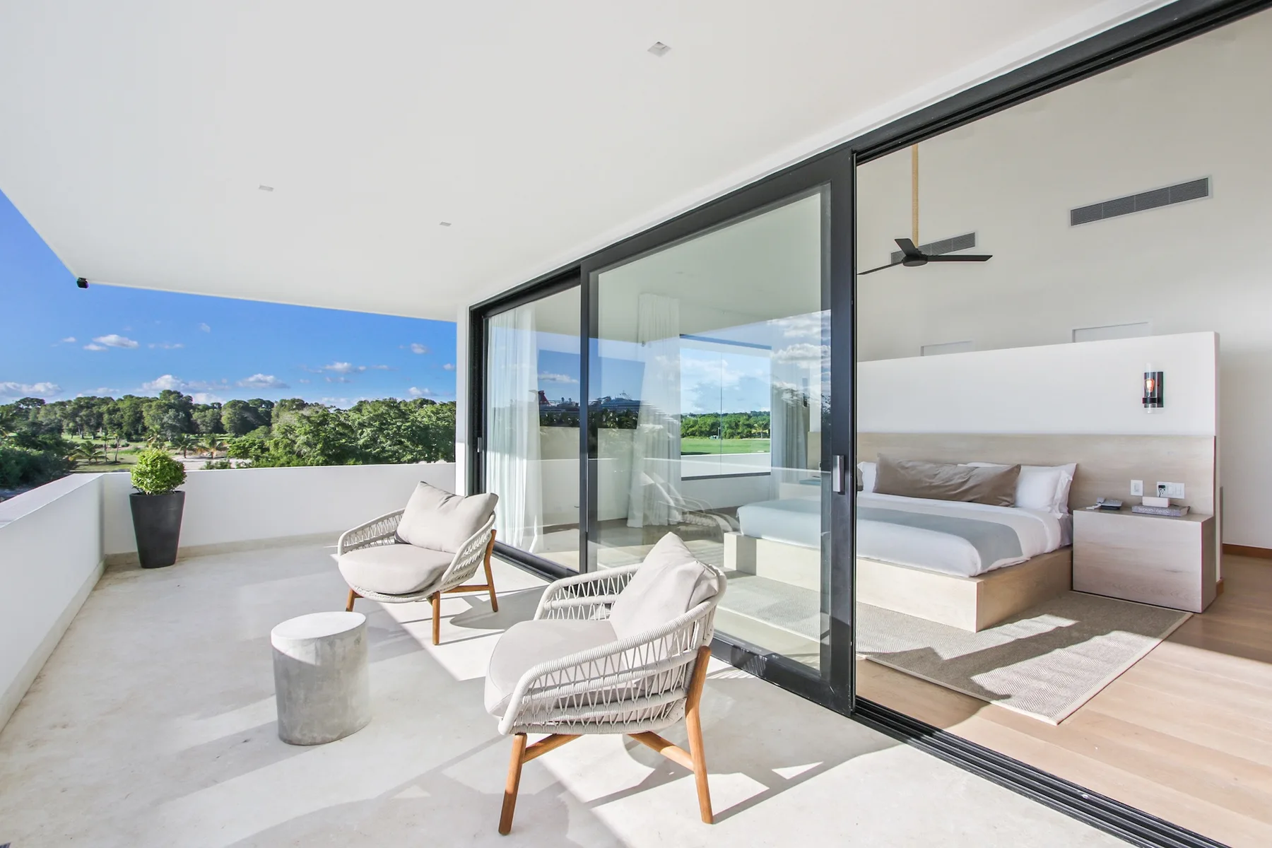 A sunny terrace with two seats overlooks a green landscape beside a bedroom.