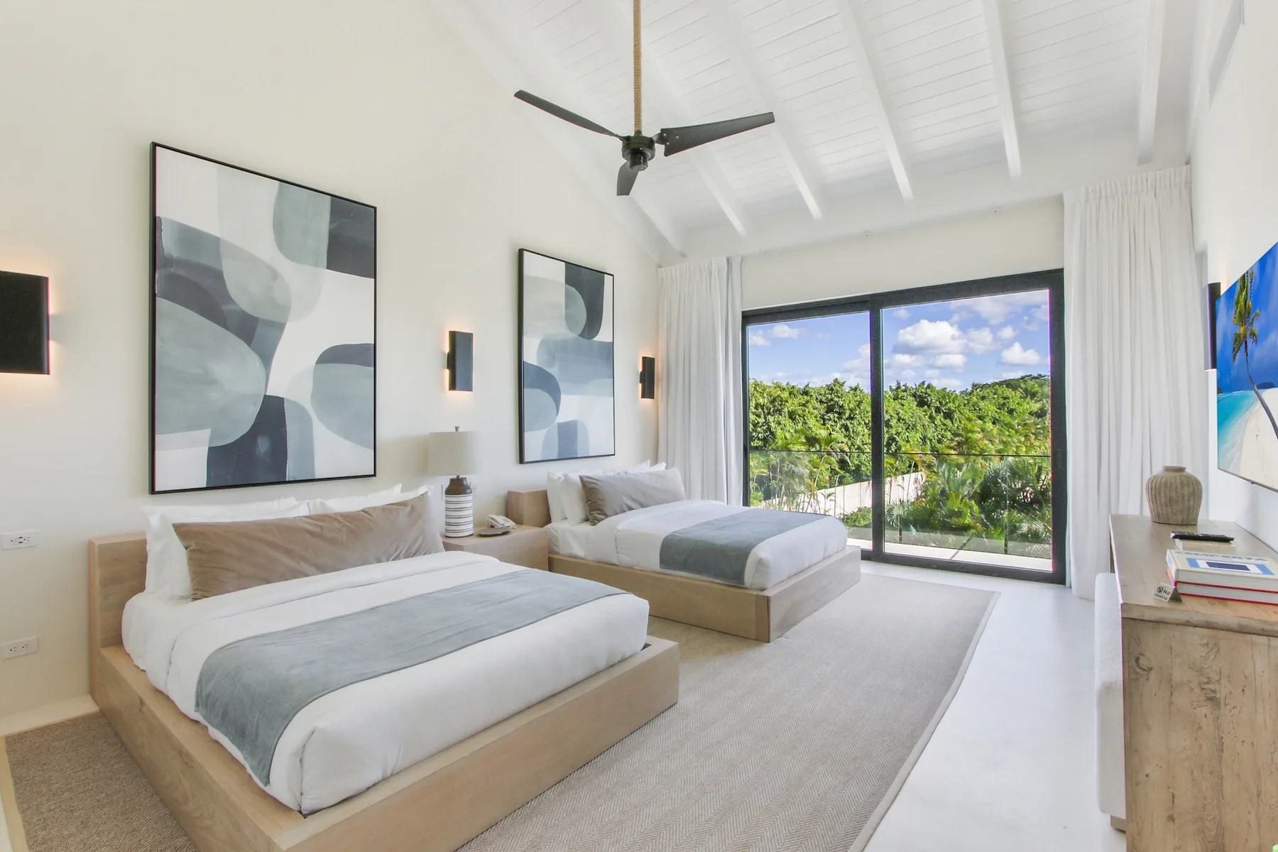 A bright bedroom with two beds and sliding glass doors opening onto greenery.