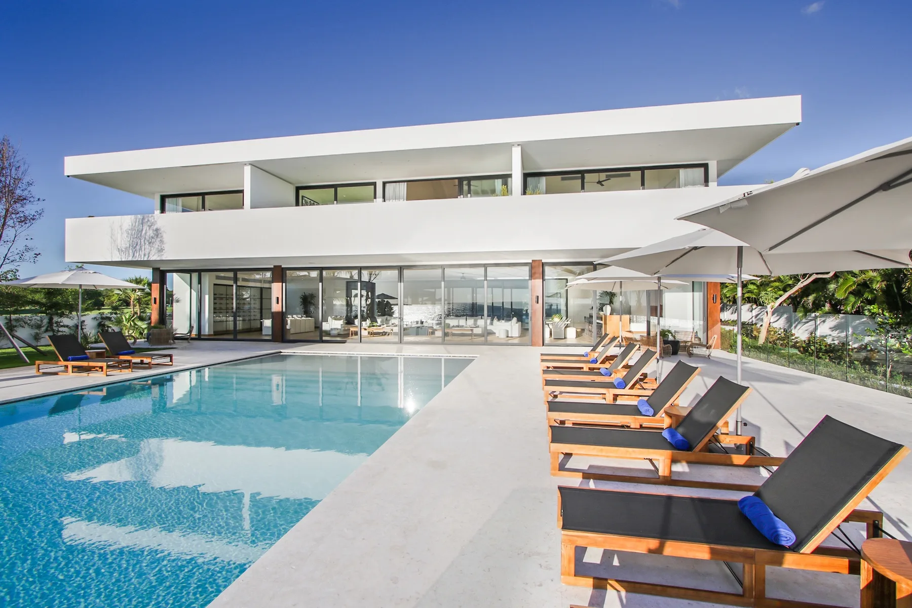 A modern house opens onto a swimming pool with lounge seating along the deck.