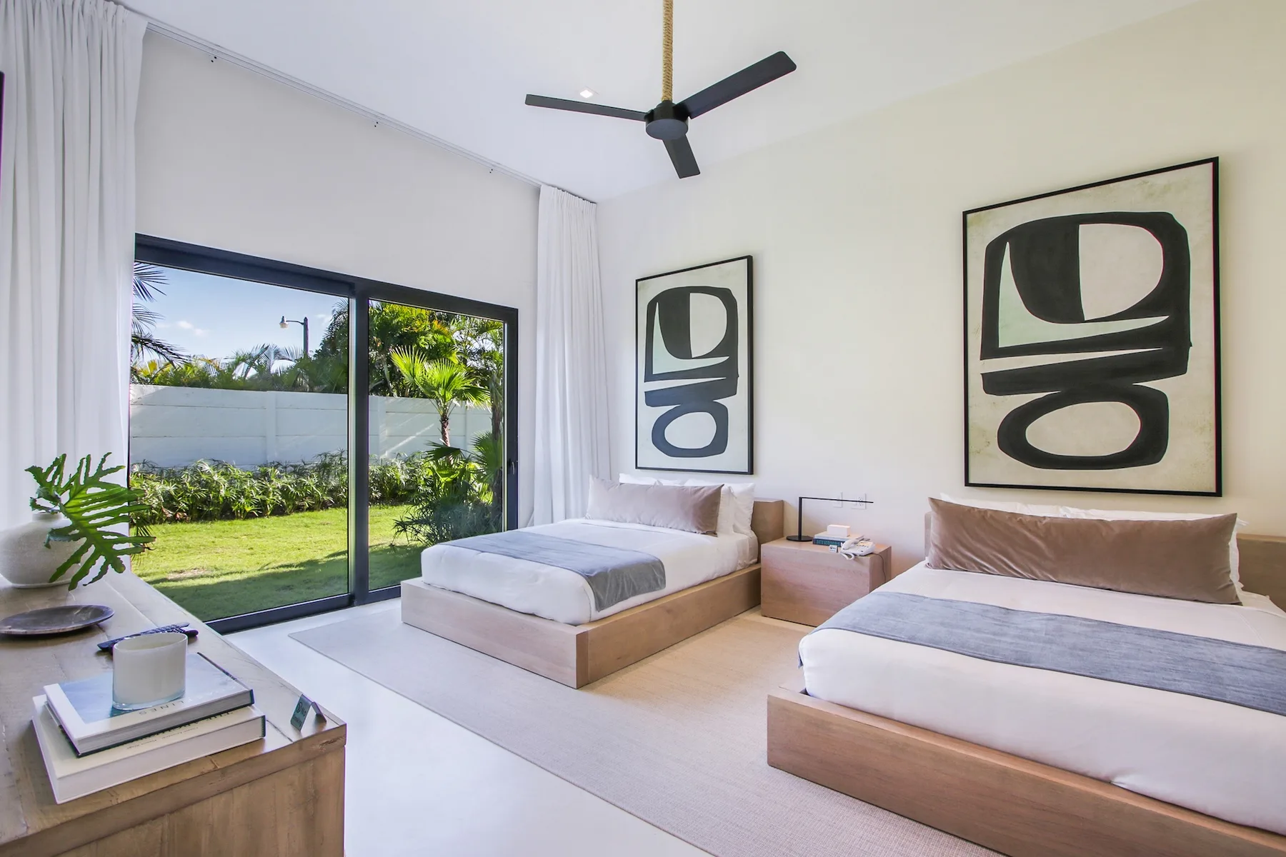 A bright bedroom with two beds, large windows, and views of a garden.
