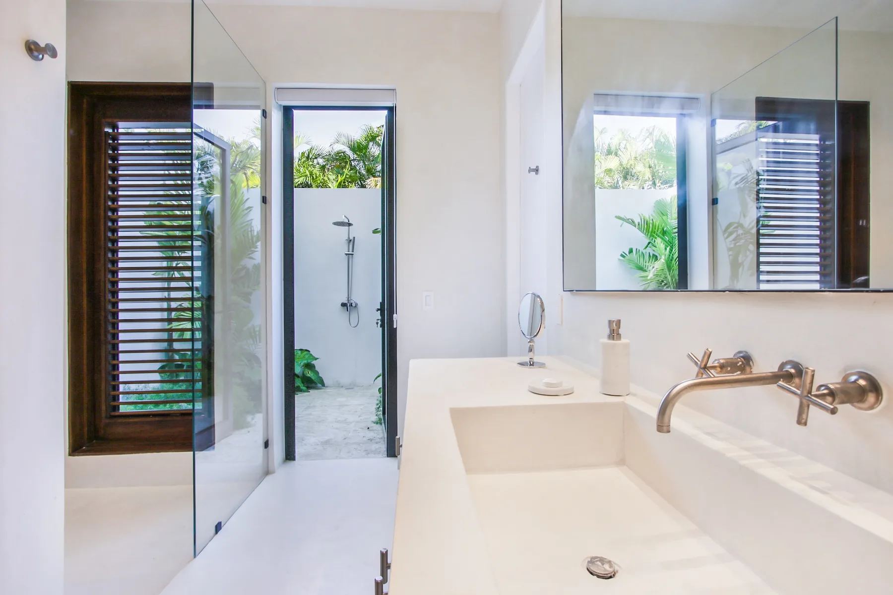 A bright bathroom with a shower, a large sink, and windows overlooking greenery.