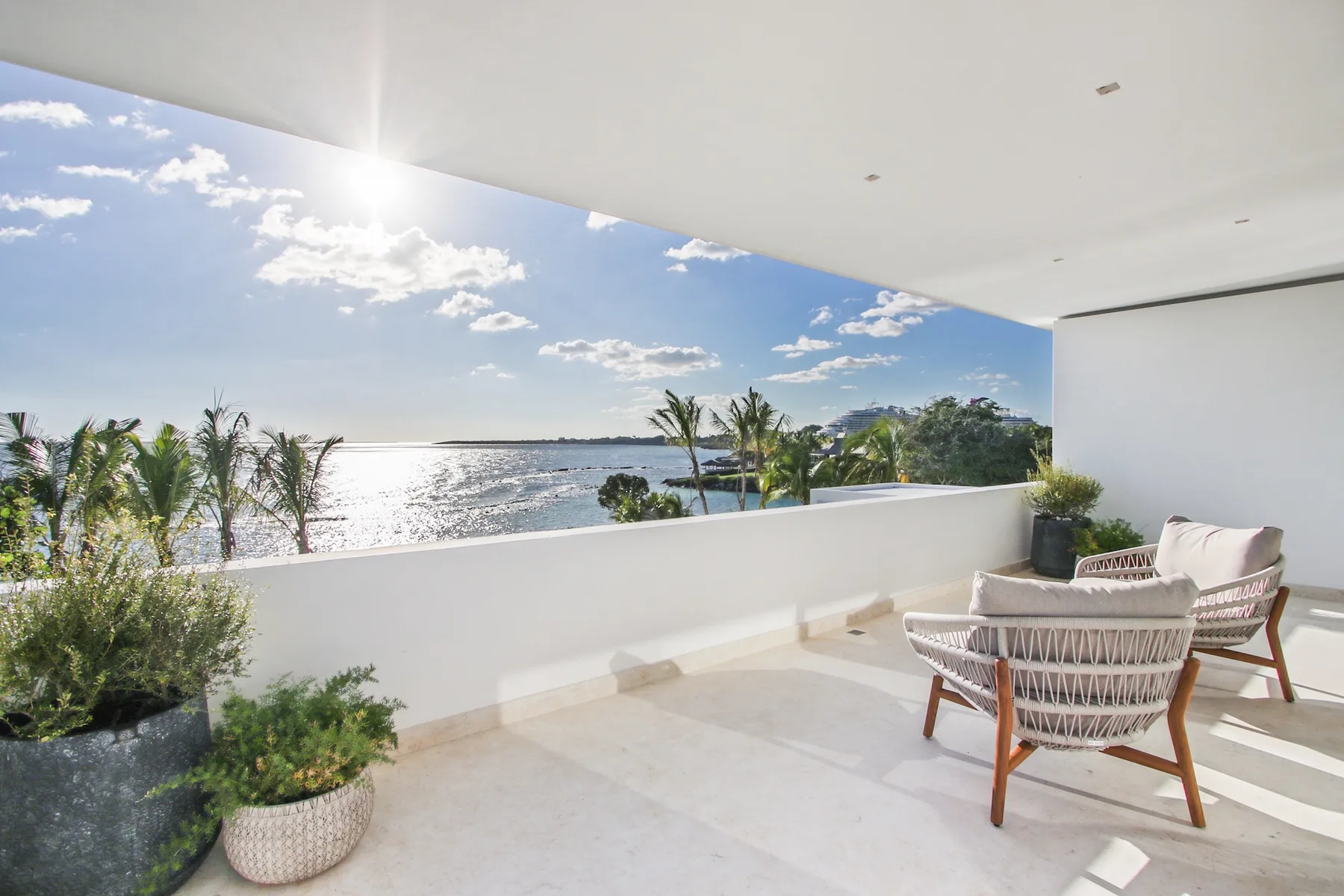 A covered terrace with seating overlooks the water and palm trees.