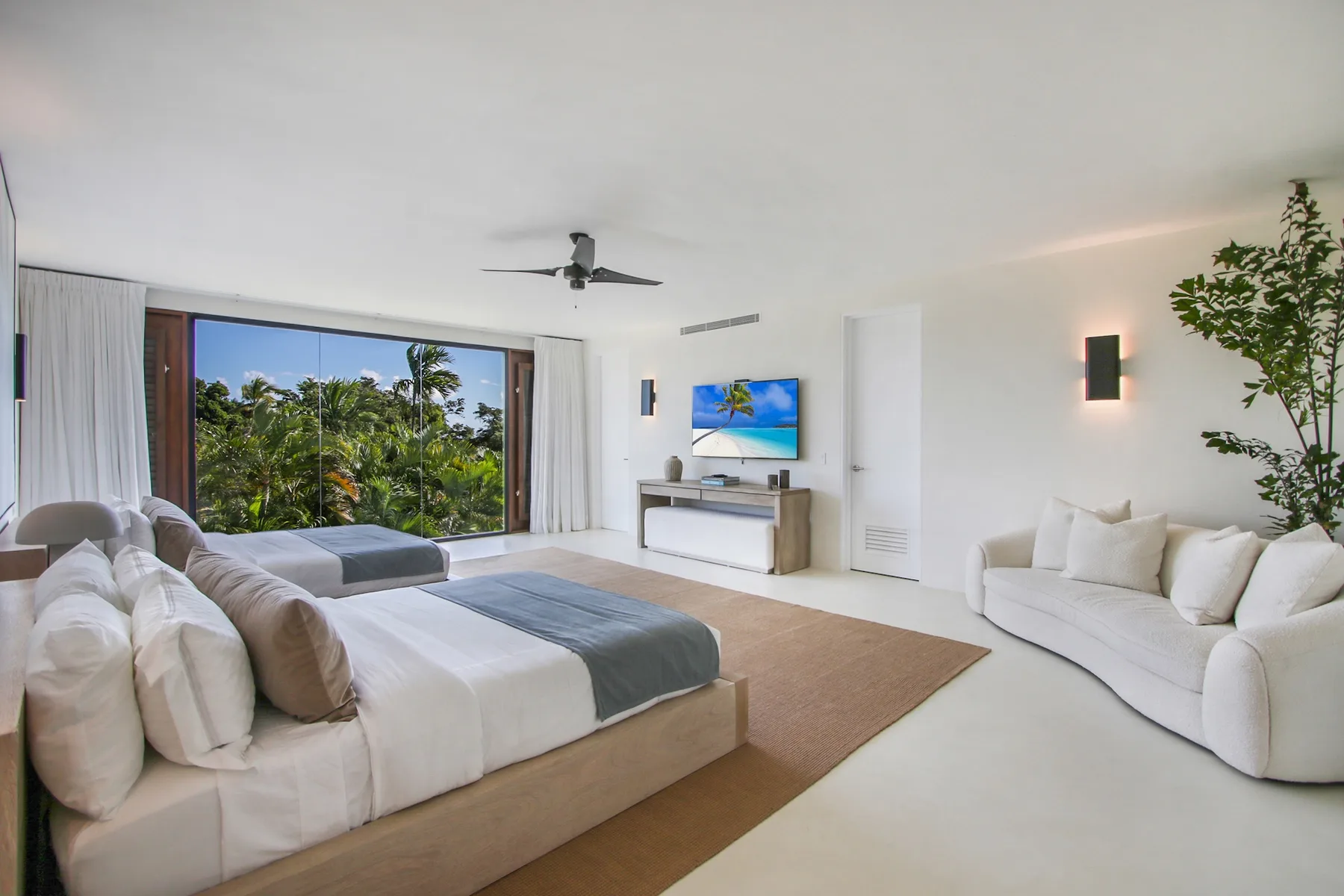 A bright bedroom with a bed, white seating, and a large window overlooking greenery.