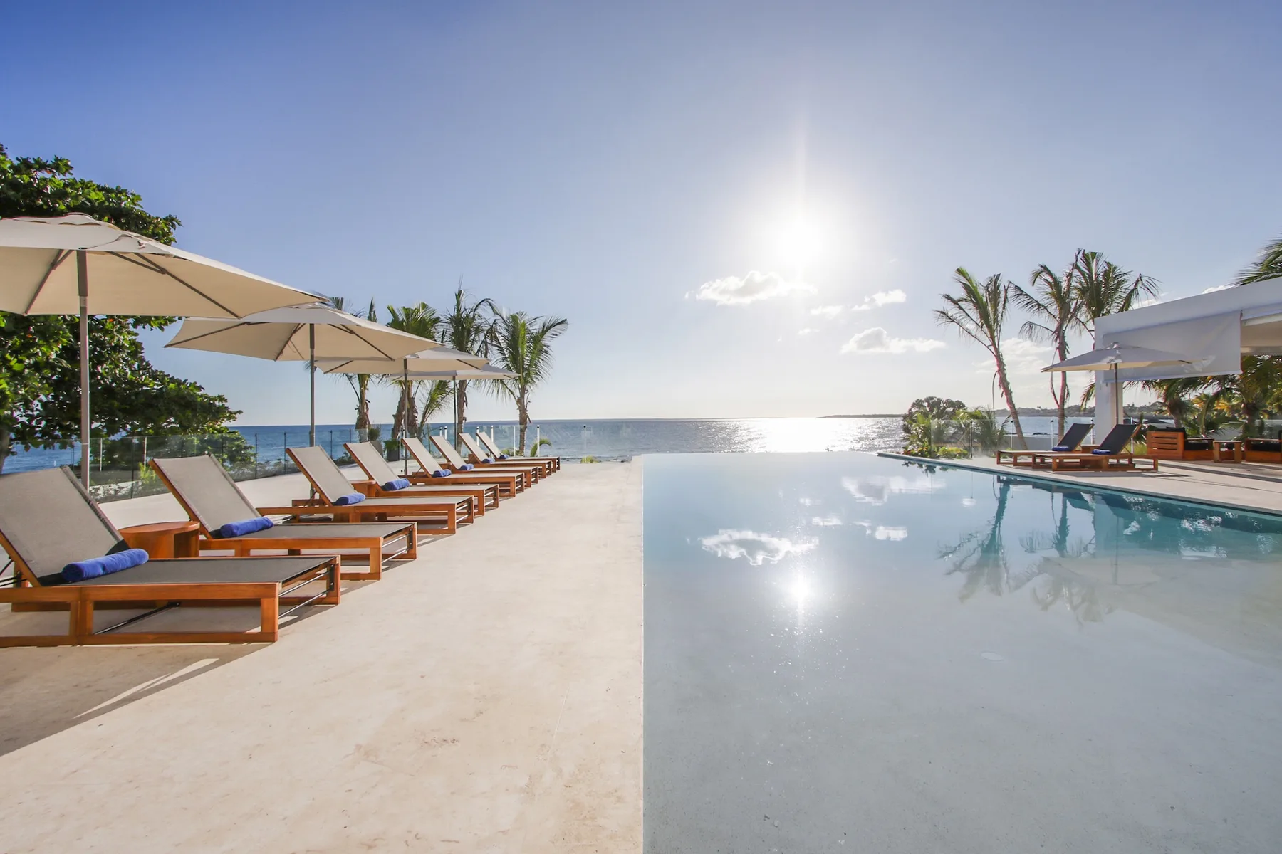 An outdoor pool beside a row of loungers and umbrellas, with the ocean beyond.