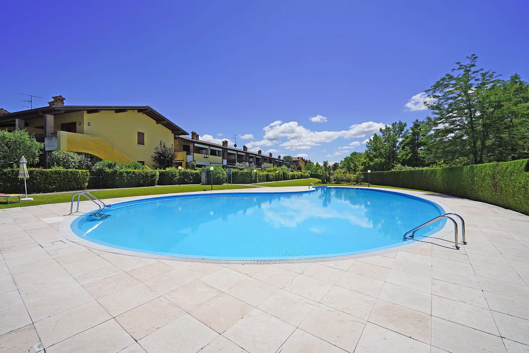 An outdoor swimming pool sits beside a paved deck and landscaped greenery.