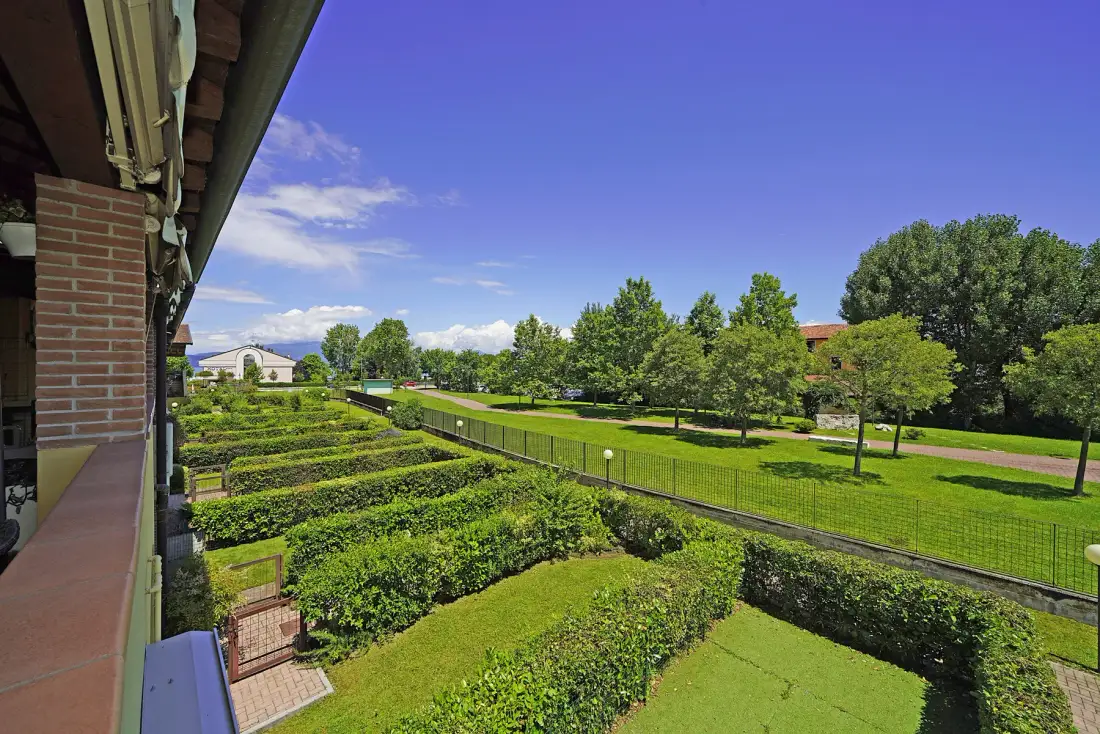 A landscaped garden with rows of hedges and a fenced green lawn beneath a blue sky.
