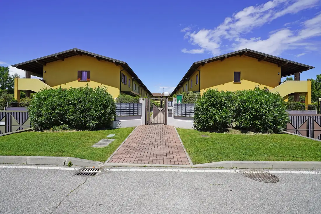 A pair of yellow residential buildings flank a paved walkway leading to a central gate.