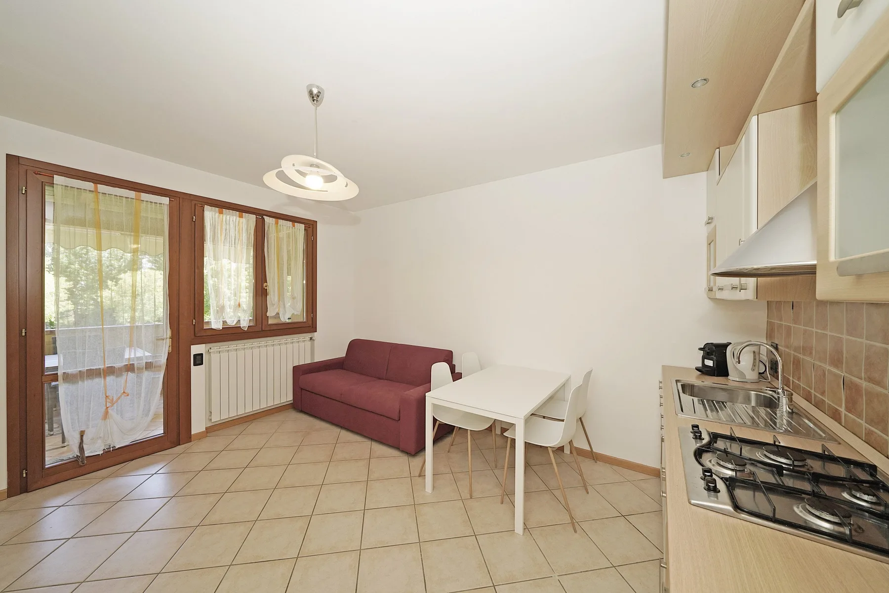 A compact room combines a small seating area, dining table, and kitchen.