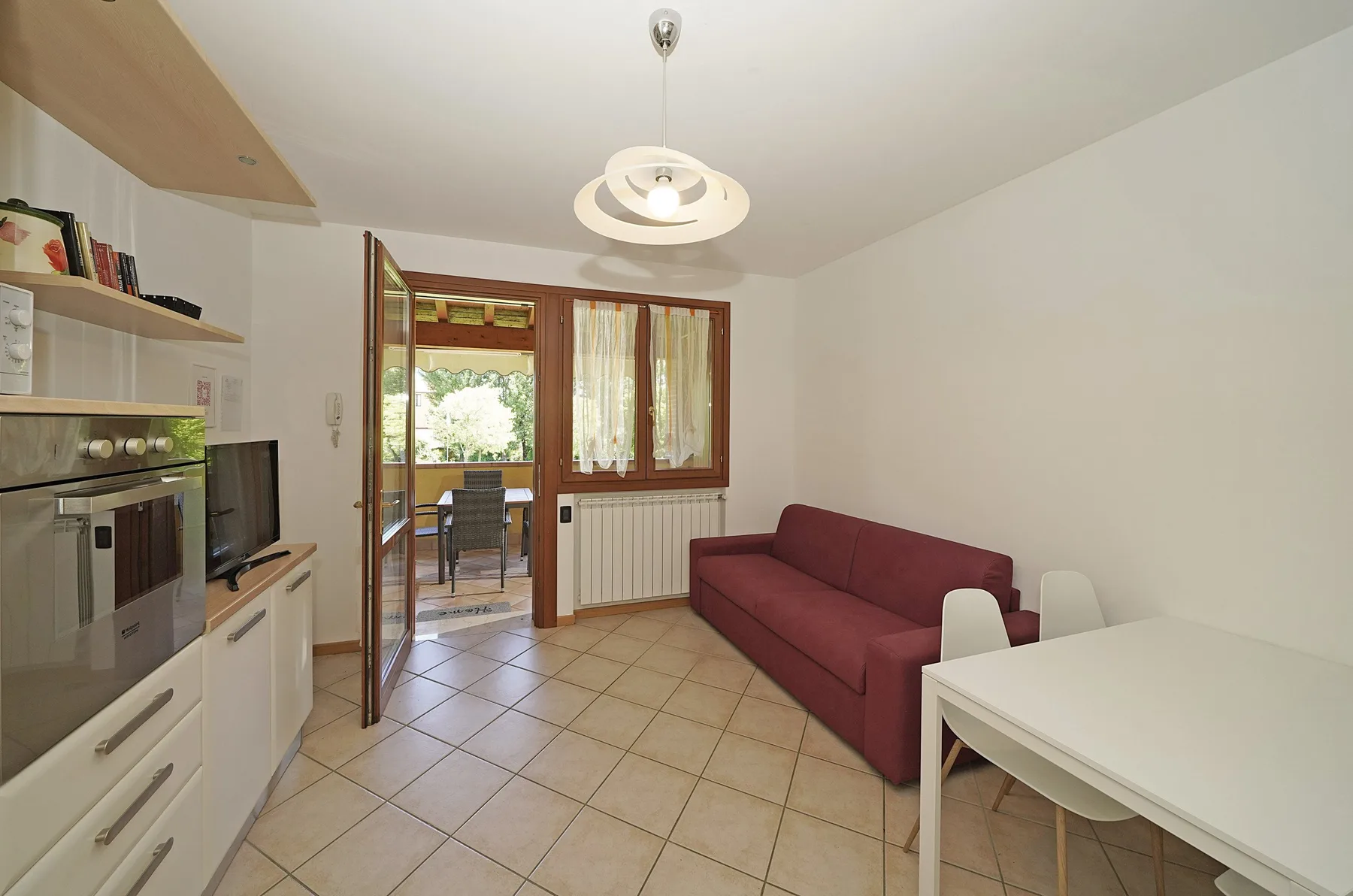 A bright living and dining area with a burgundy sofa and a white table.