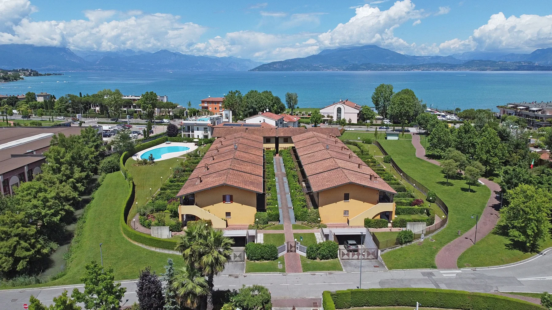 A landscaped lakeside property with two buildings, gardens, and a swimming pool.