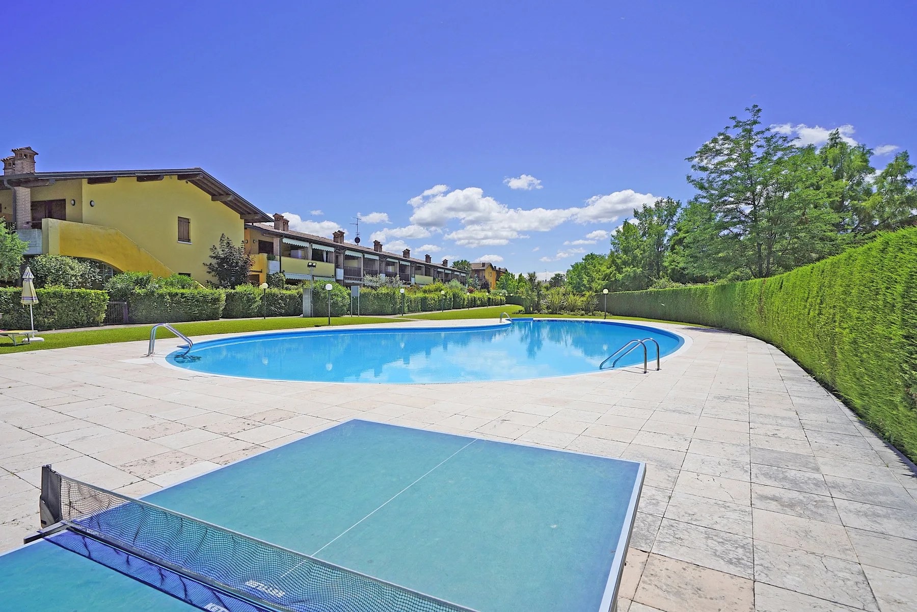 An outdoor swimming pool and table tennis table sit beside landscaped grounds.