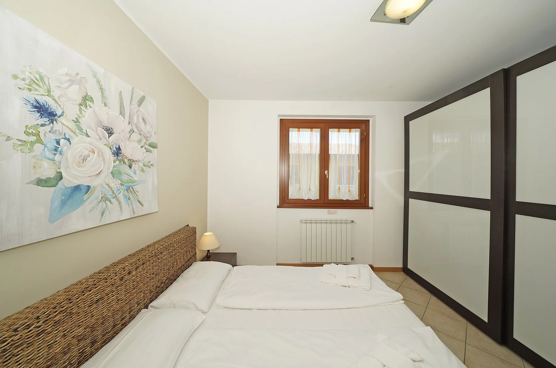 A bedroom with a bed, floral wall art, and a window.