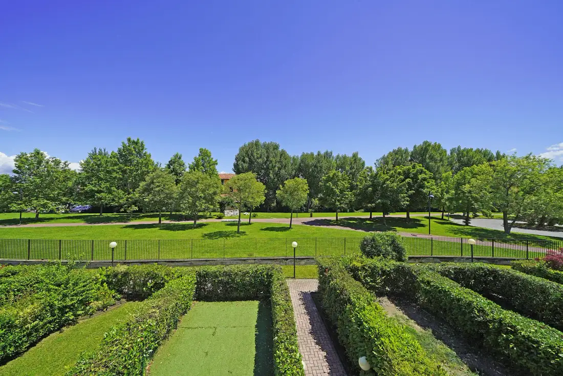 A landscaped garden has clipped hedges, a paved path, and a broad green lawn.