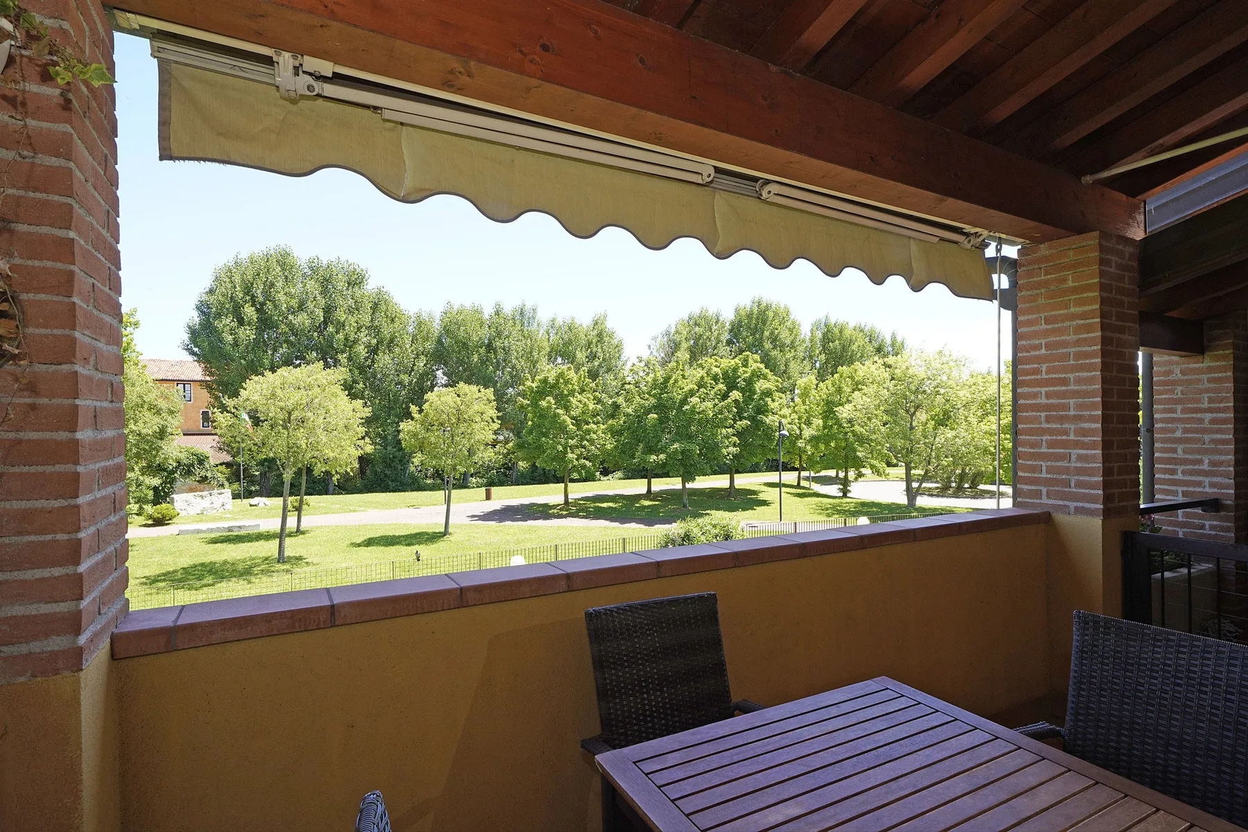A covered patio overlooks a grassy park with trees.
