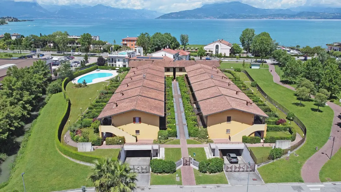 Aerial view of a landscaped resort complex beside a lake, with a pool and gardens.