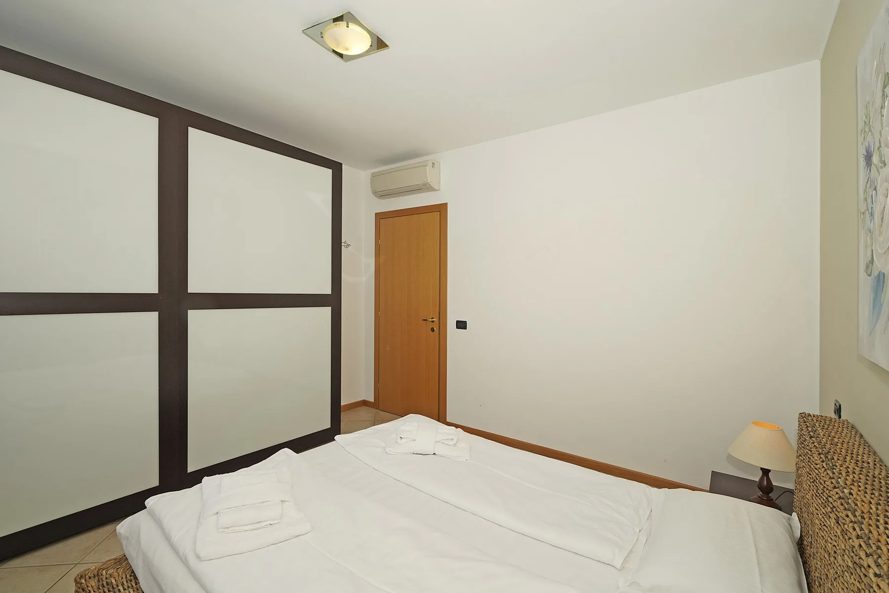 A bedroom with a bed, a wooden door, and a wall-mounted air conditioner.
