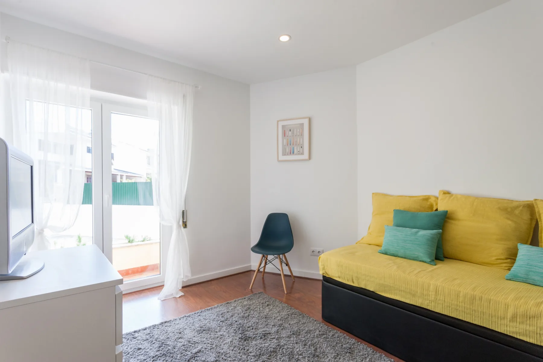 Un dormitorio luminoso con una cama amarilla y una ventana con cortinas translúcidas.