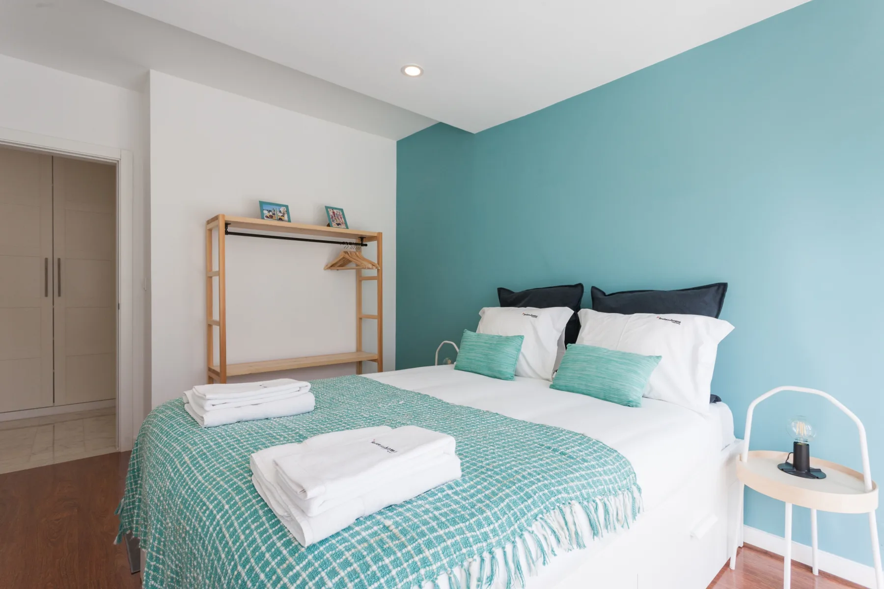 Un dormitorio con una cama vestida con ropa blanca y una colcha verde azulado.