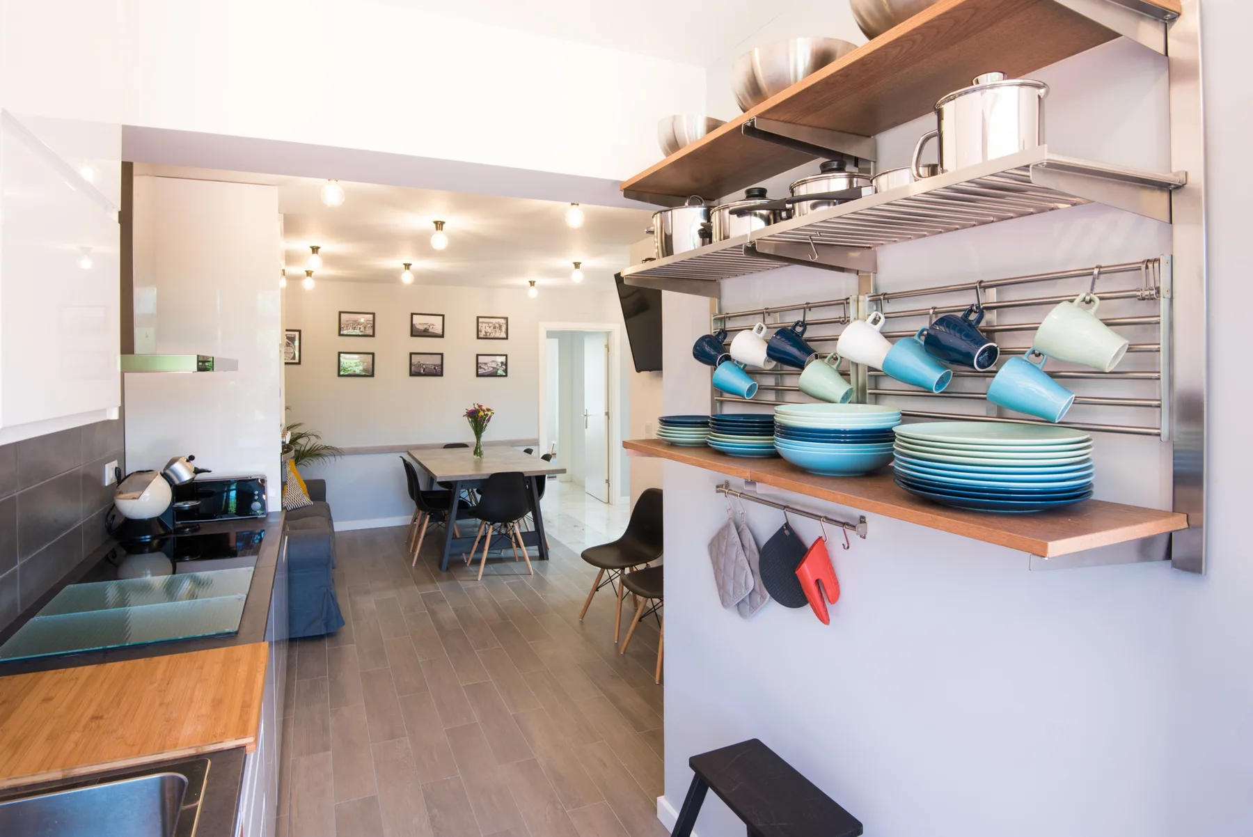 Una cocina luminosa con estantes abiertos de vajilla y un comedor al fondo.