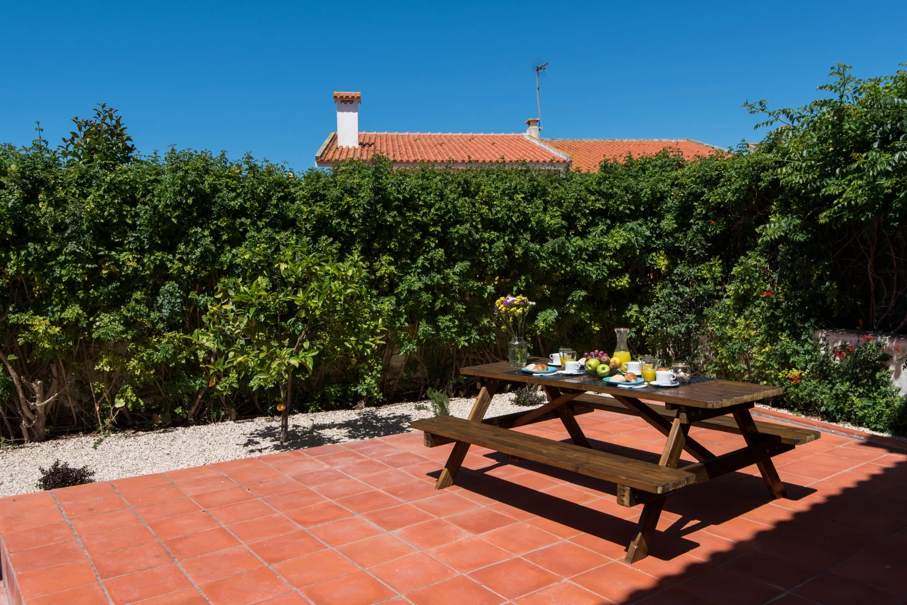 Un patio ajardinado con una mesa de madera preparada para comer.