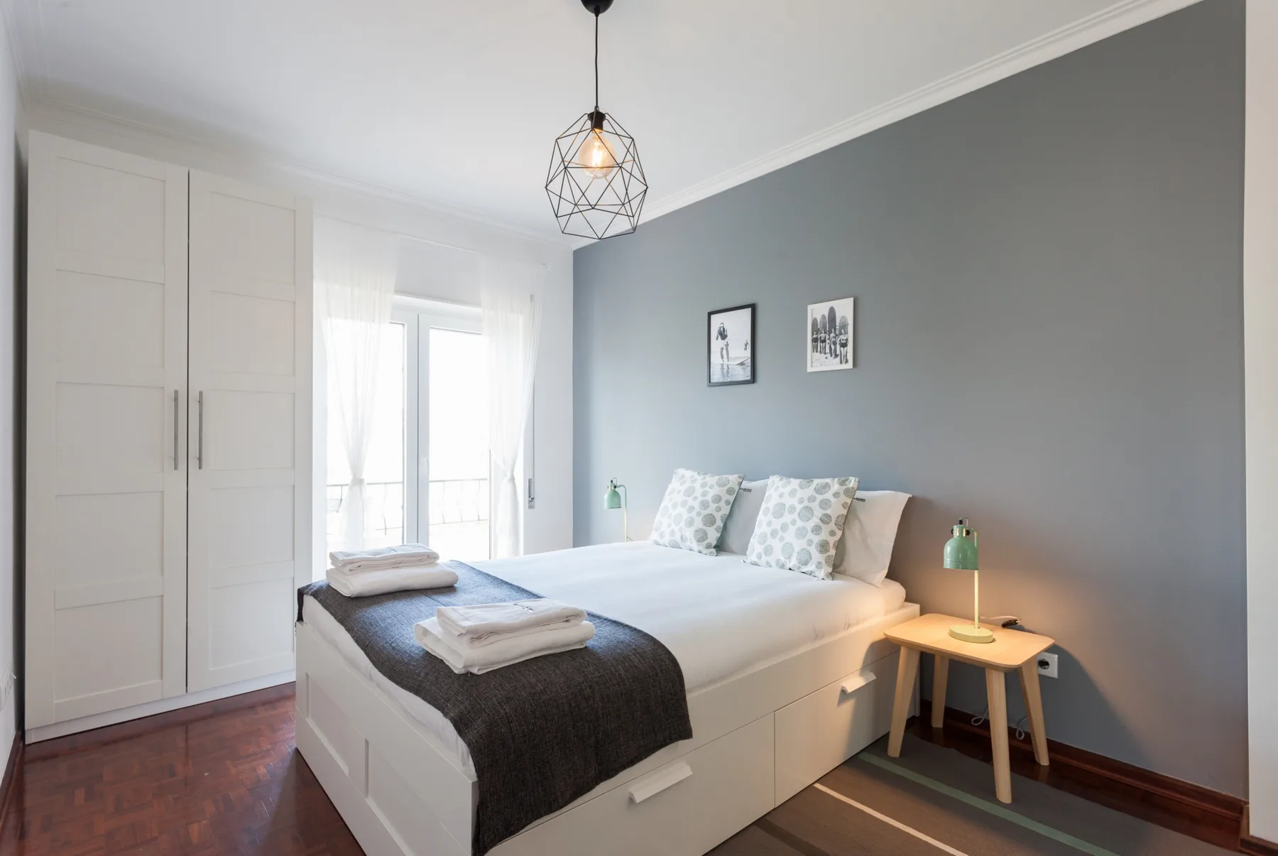 Un dormitorio luminoso con una cama blanca, una mesita de noche y un armario.