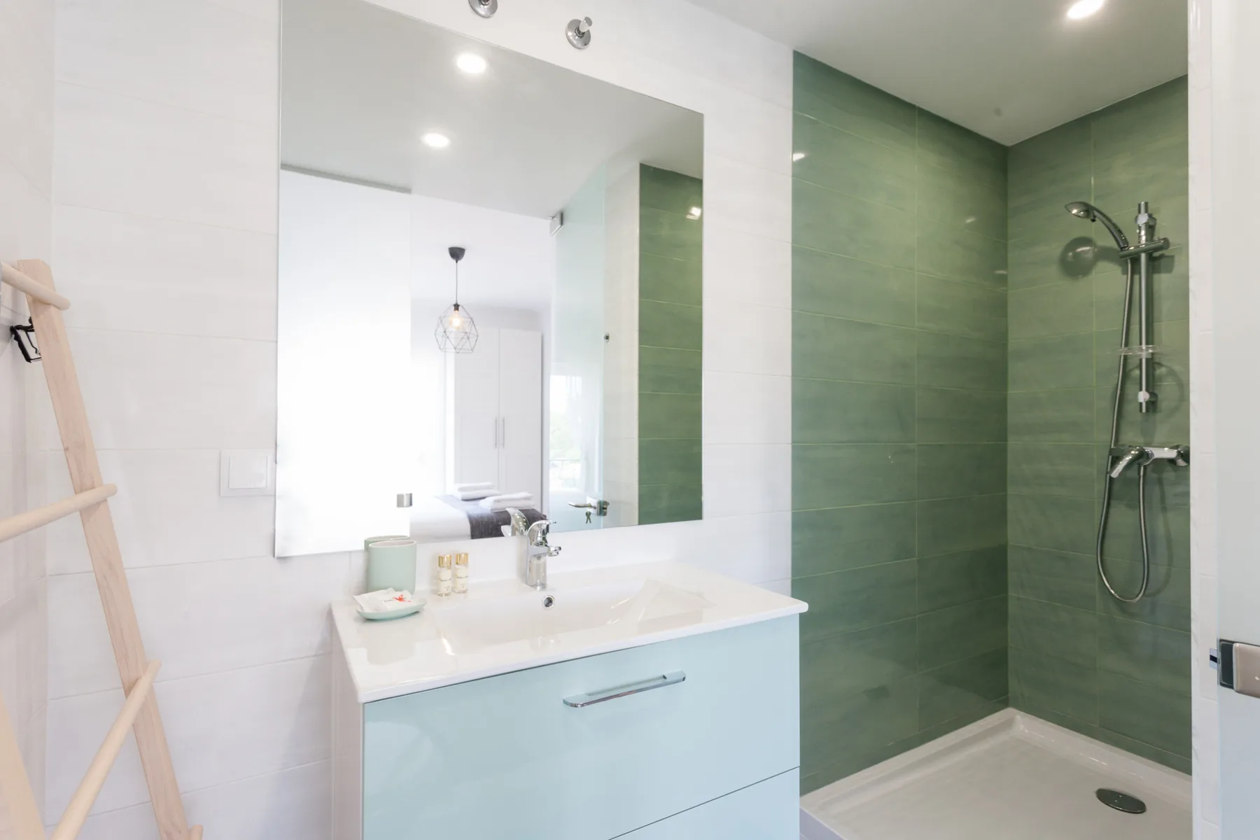 Un baño luminoso con lavabo, espejo grande y ducha con azulejos verdes.