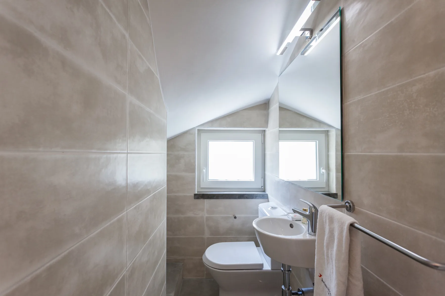 Un baño alicatado con lavabo, inodoro y dos ventanas.