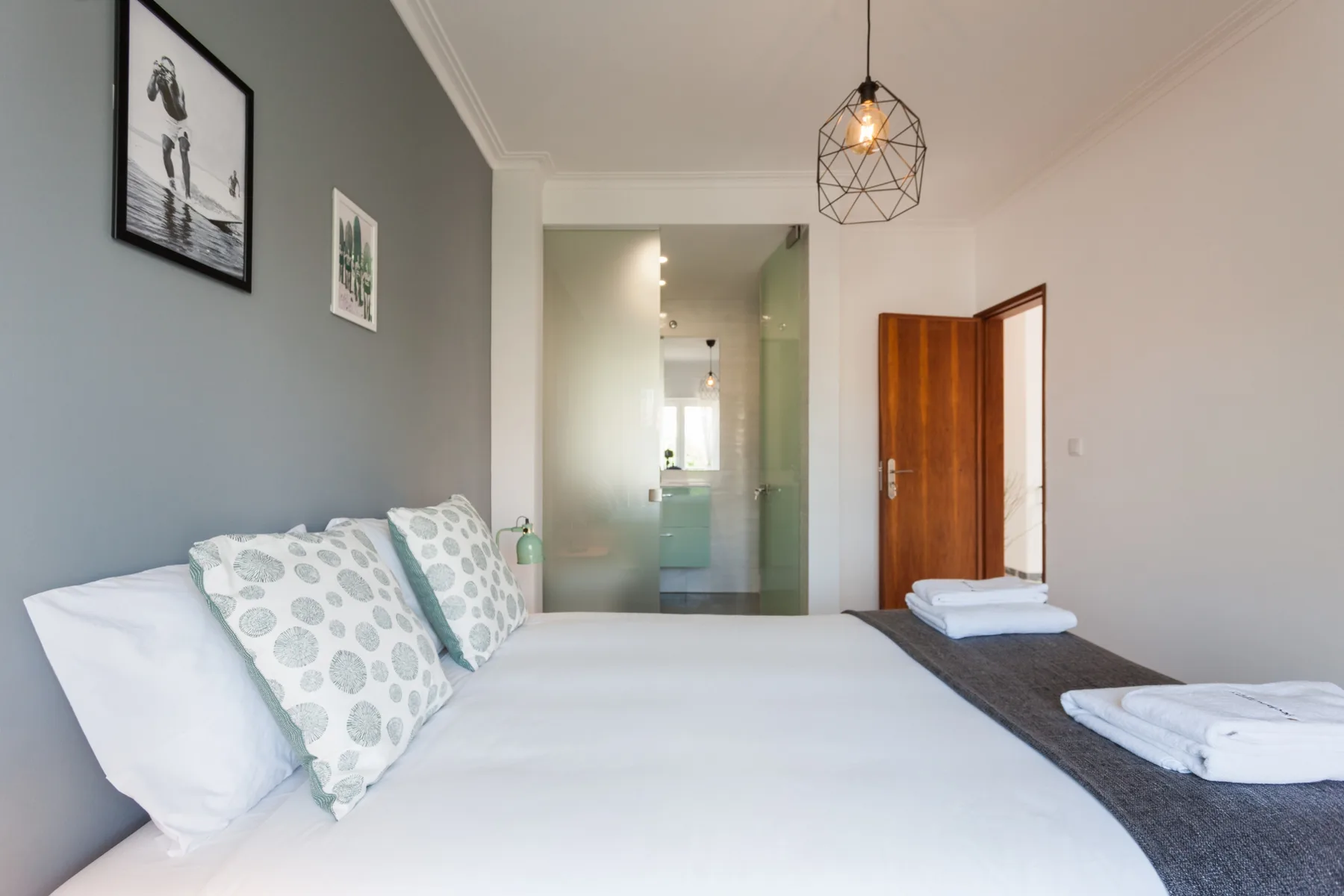 Un dormitorio con una cama bien tendida y una puerta abierta hacia otra habitación.