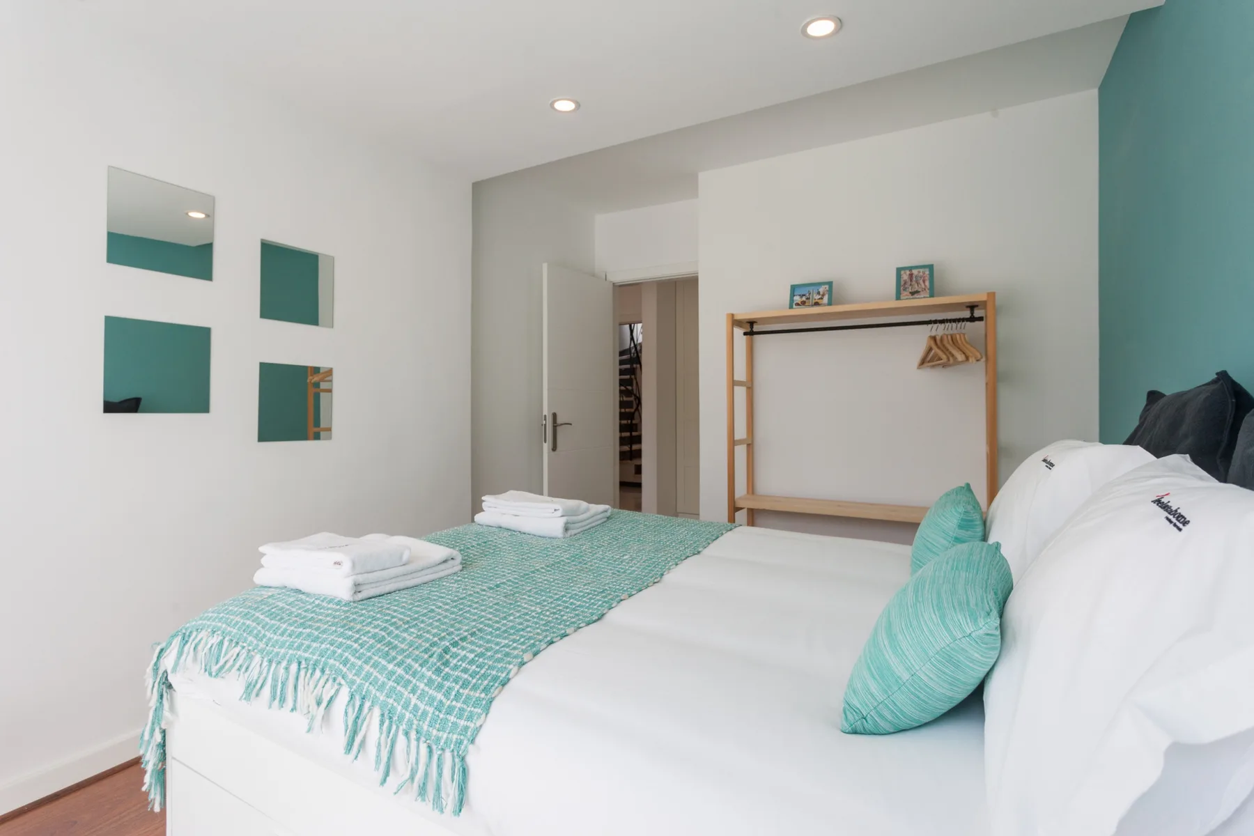 Un dormitorio luminoso con ropa de cama blanca y una manta turquesa.