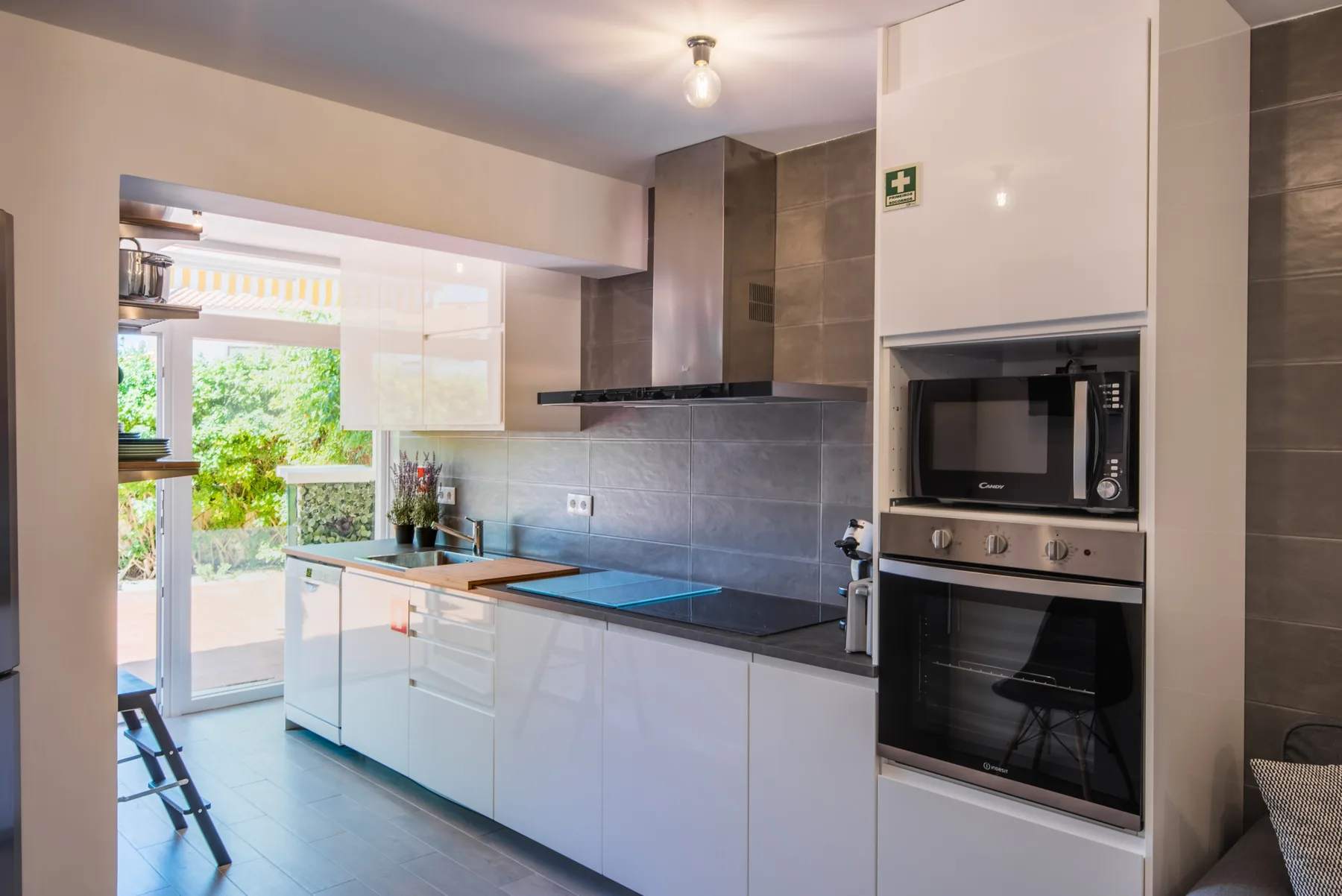 Una cocina moderna con armarios blancos y una encimera junto a una puerta acristalada luminosa.